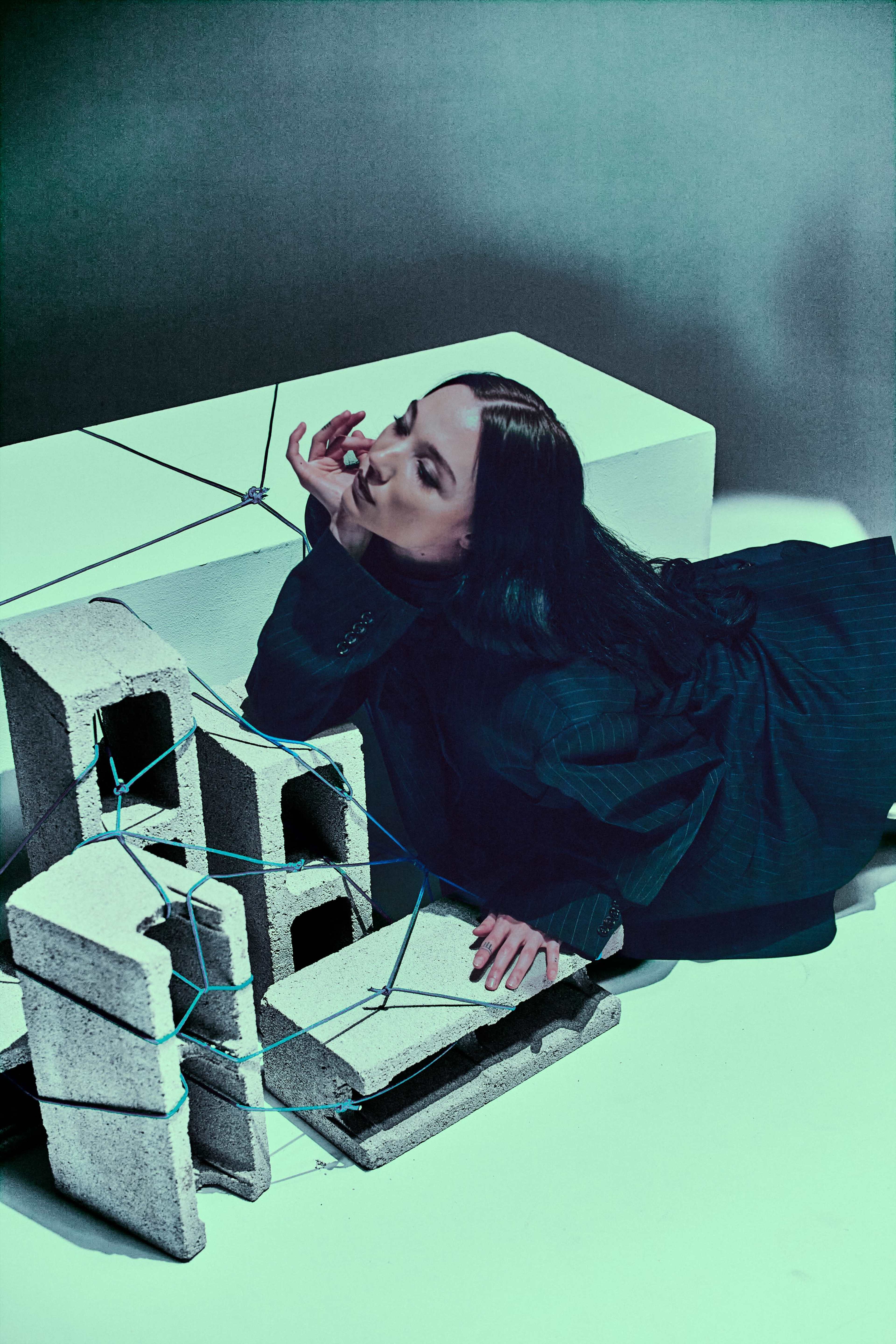 A person in a black outfit is lying beside a stack of cinder blocks, which are bound together with blue string.