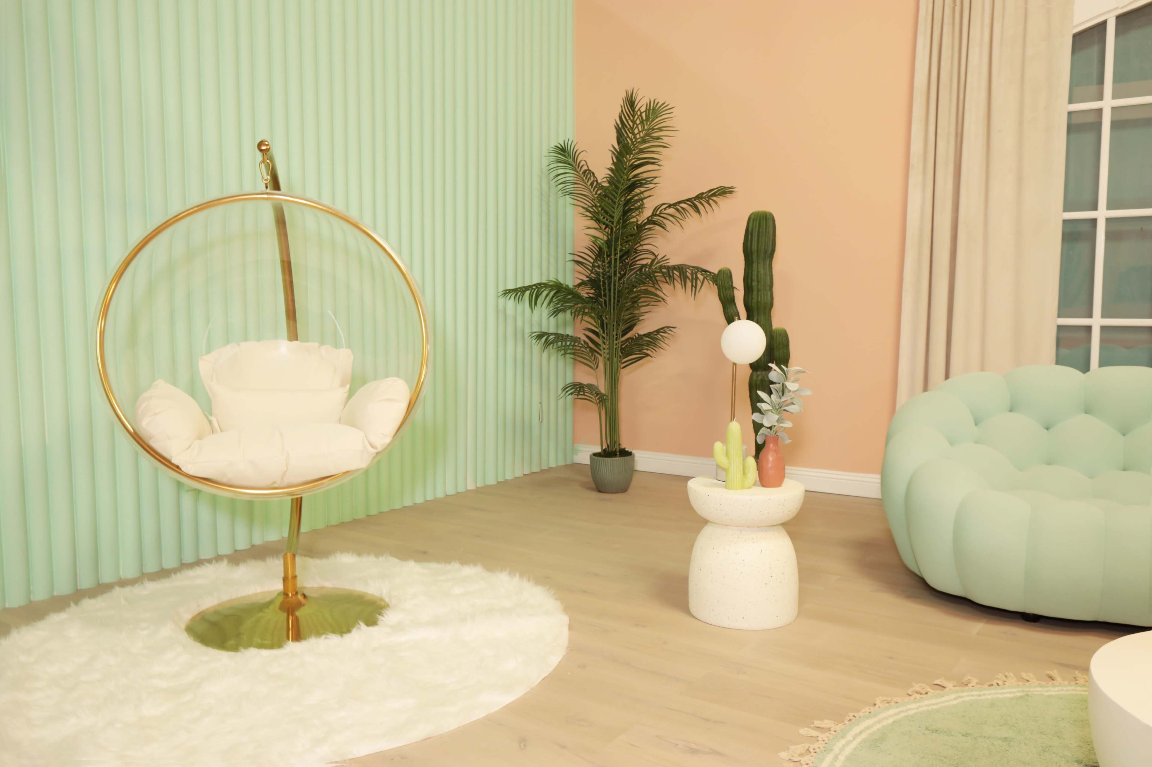 A modern interior with a hanging acrylic chair, a potted palm plant, a cactus, and a round, tufted sofa.