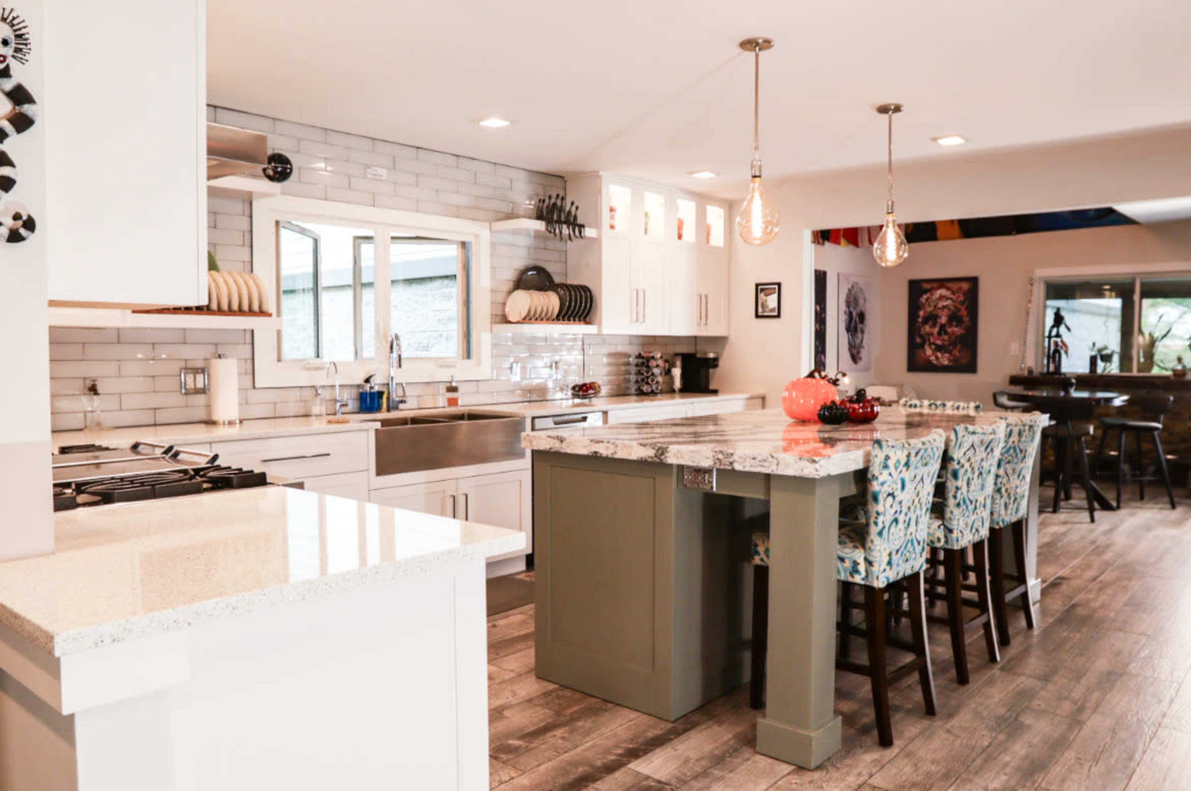 The kitchen features a large island with colorful barstools, stainless steel appliances, and modern cabinetry.