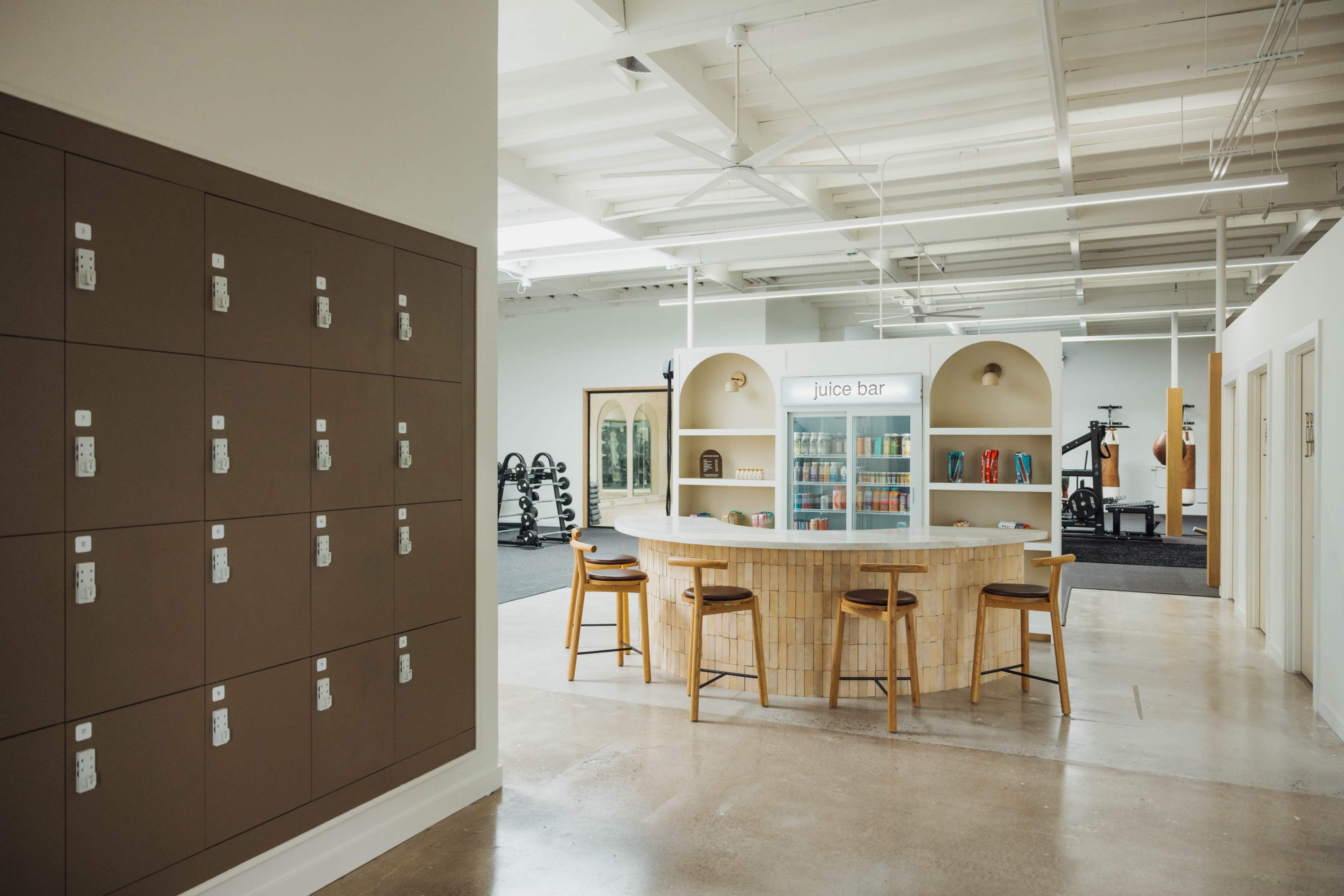 The image shows a modern gym interior with a juice bar, seating area, and locker storage on one side.