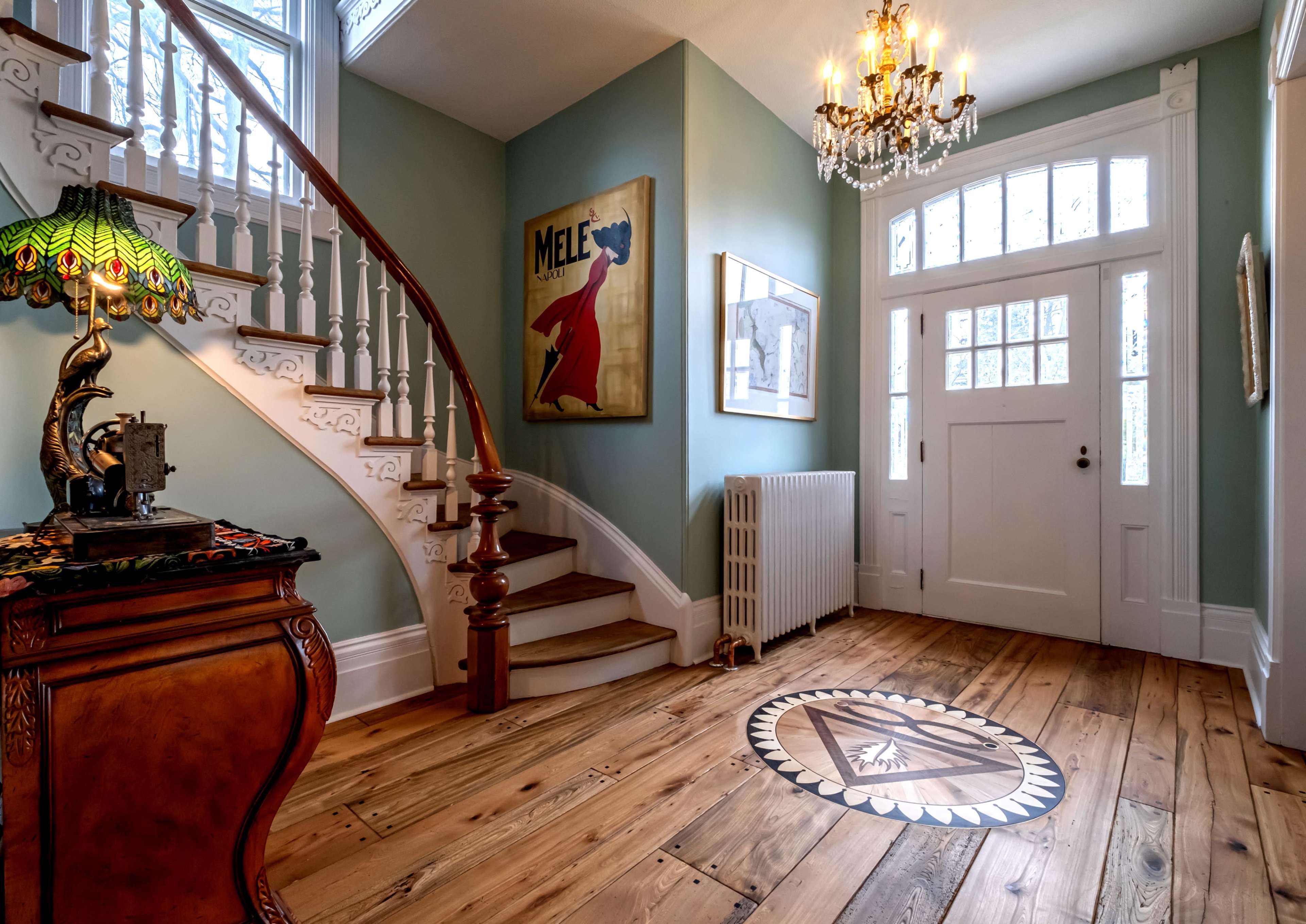 The entryway features a staircase with intricate wooden railings, a chandelier, and a decorative inlaid wooden floor.