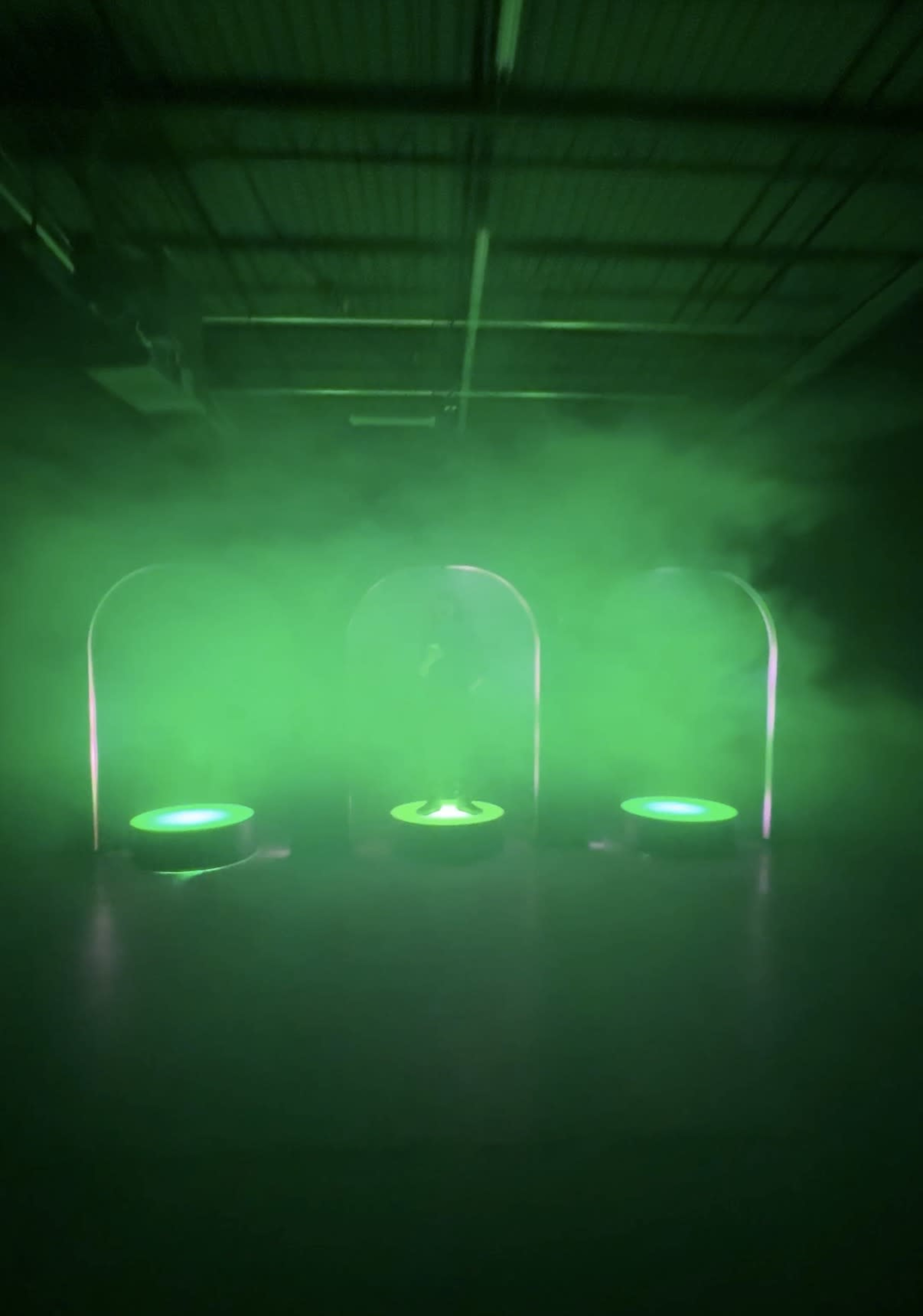 The scene features three illuminated circular platforms surrounded by a green mist and positioned under archways in a dimly lit space.