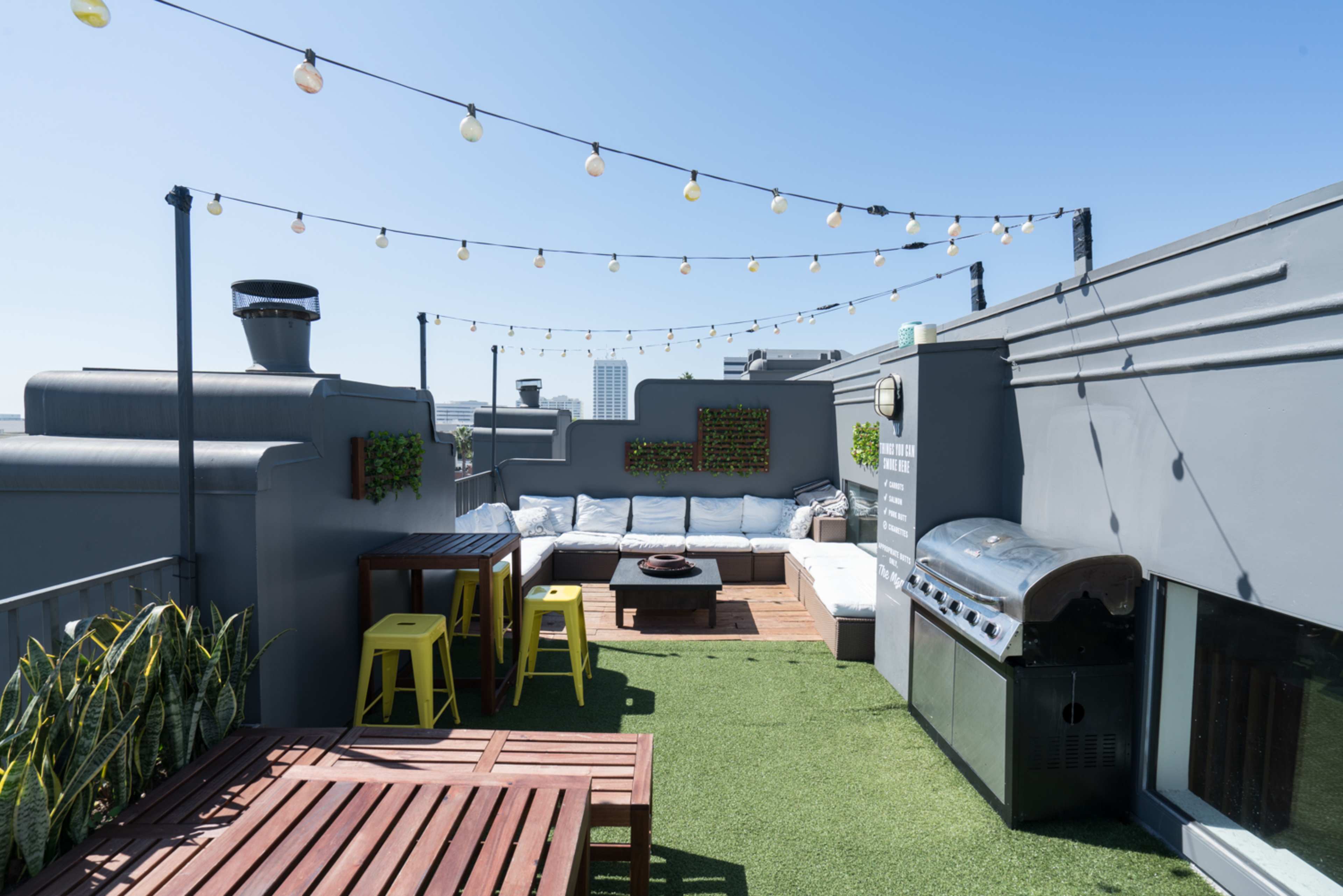 A rooftop terrace with outdoor seating, a barbecue grill, string lights, and greenery on the walls.