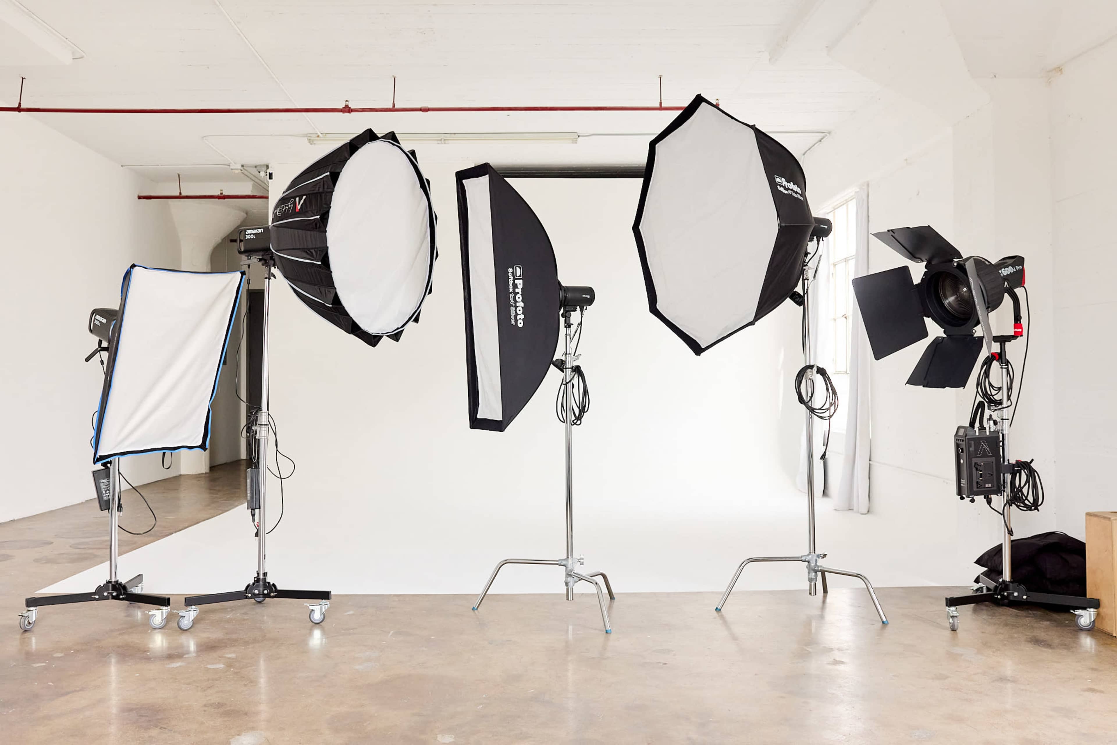 The image shows a photography studio setup featuring various softbox lights and a spotlight on stands, positioned in front of a blank backdrop.