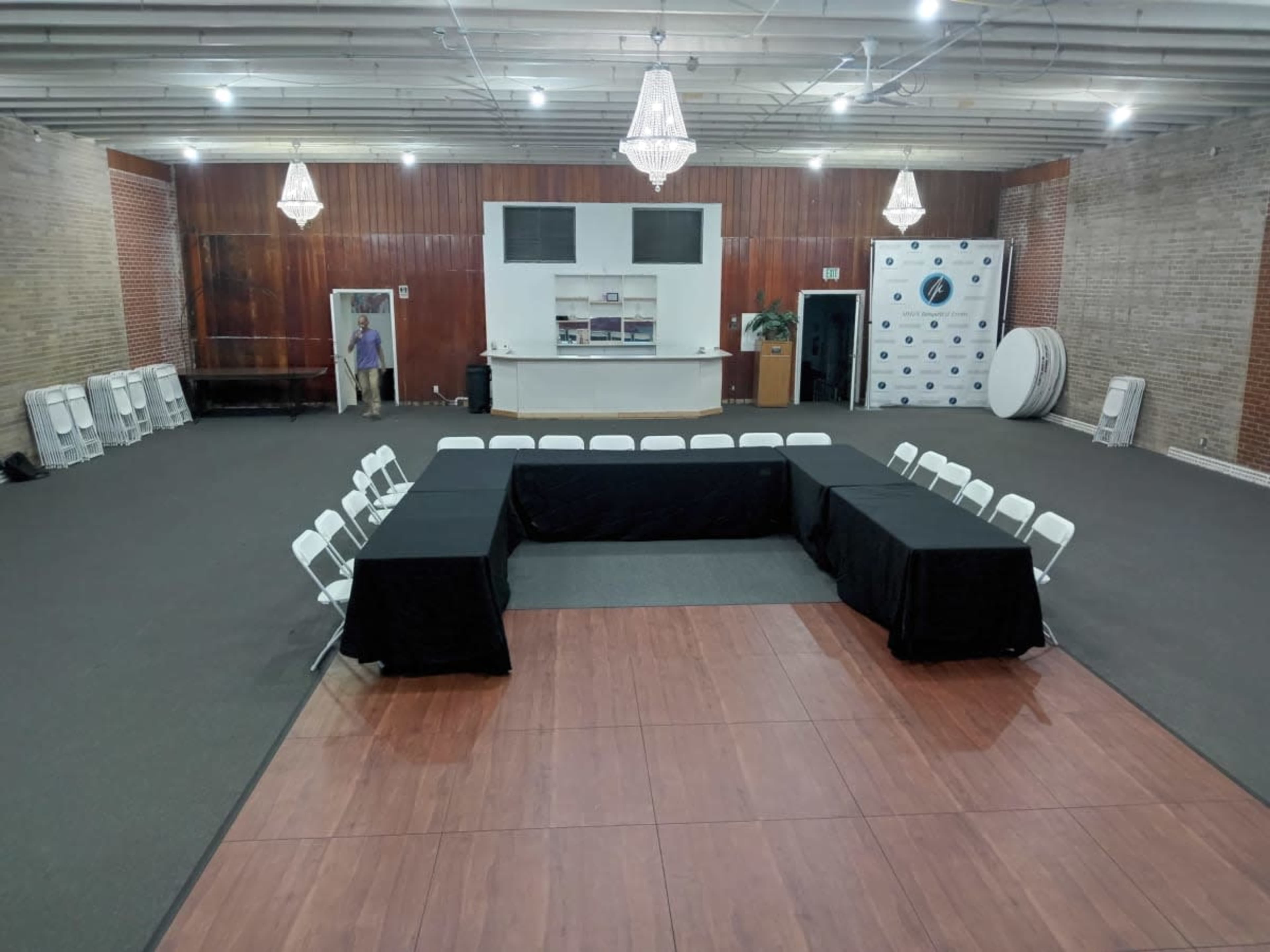 A spacious room with a flat, carpeted area featuring a rectangular arrangement of tables covered in black cloth and white chairs positioned around them.