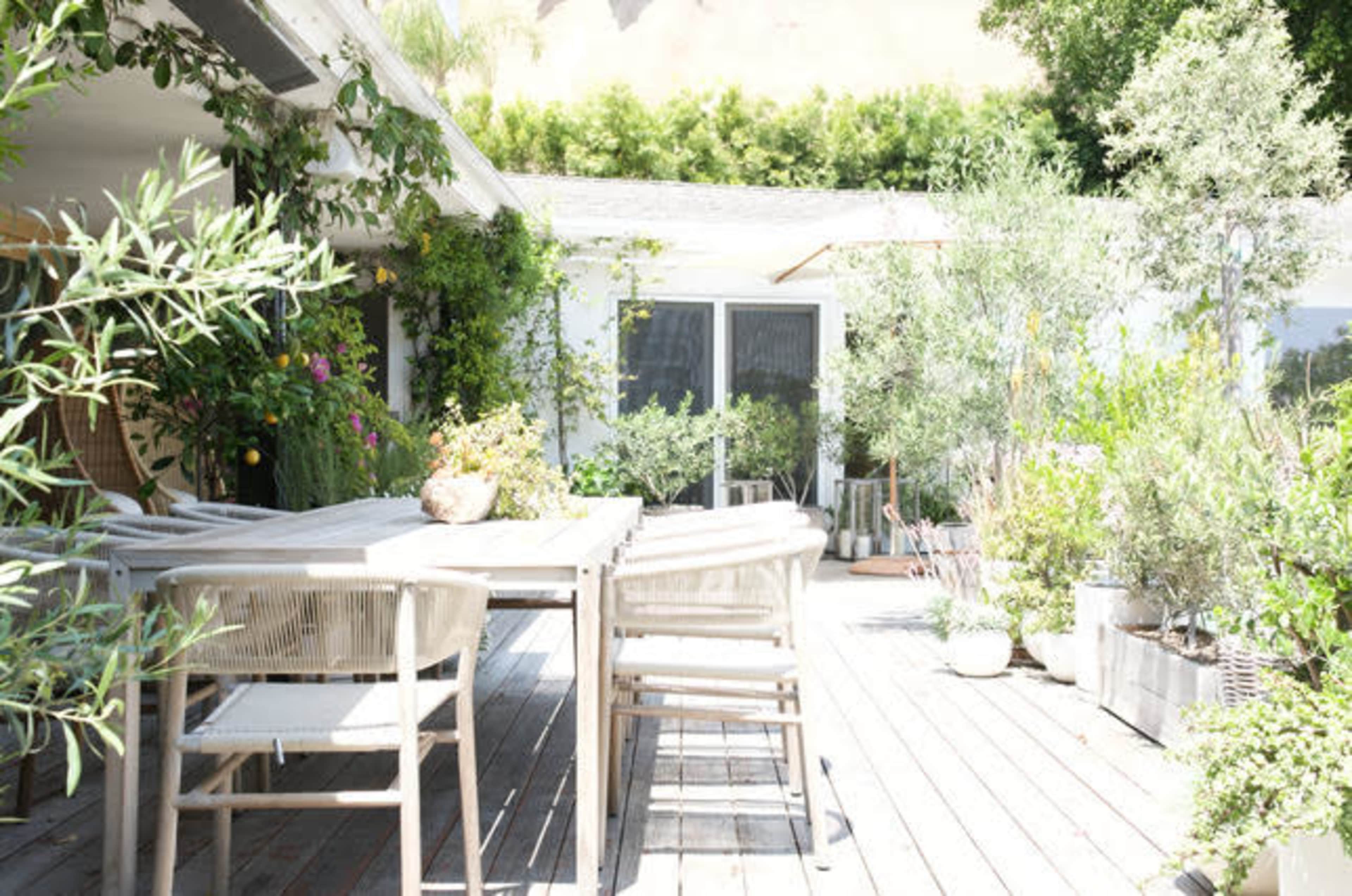 A wooden deck is surrounded by various potted plants and outdoor furniture, creating a serene outdoor dining area.