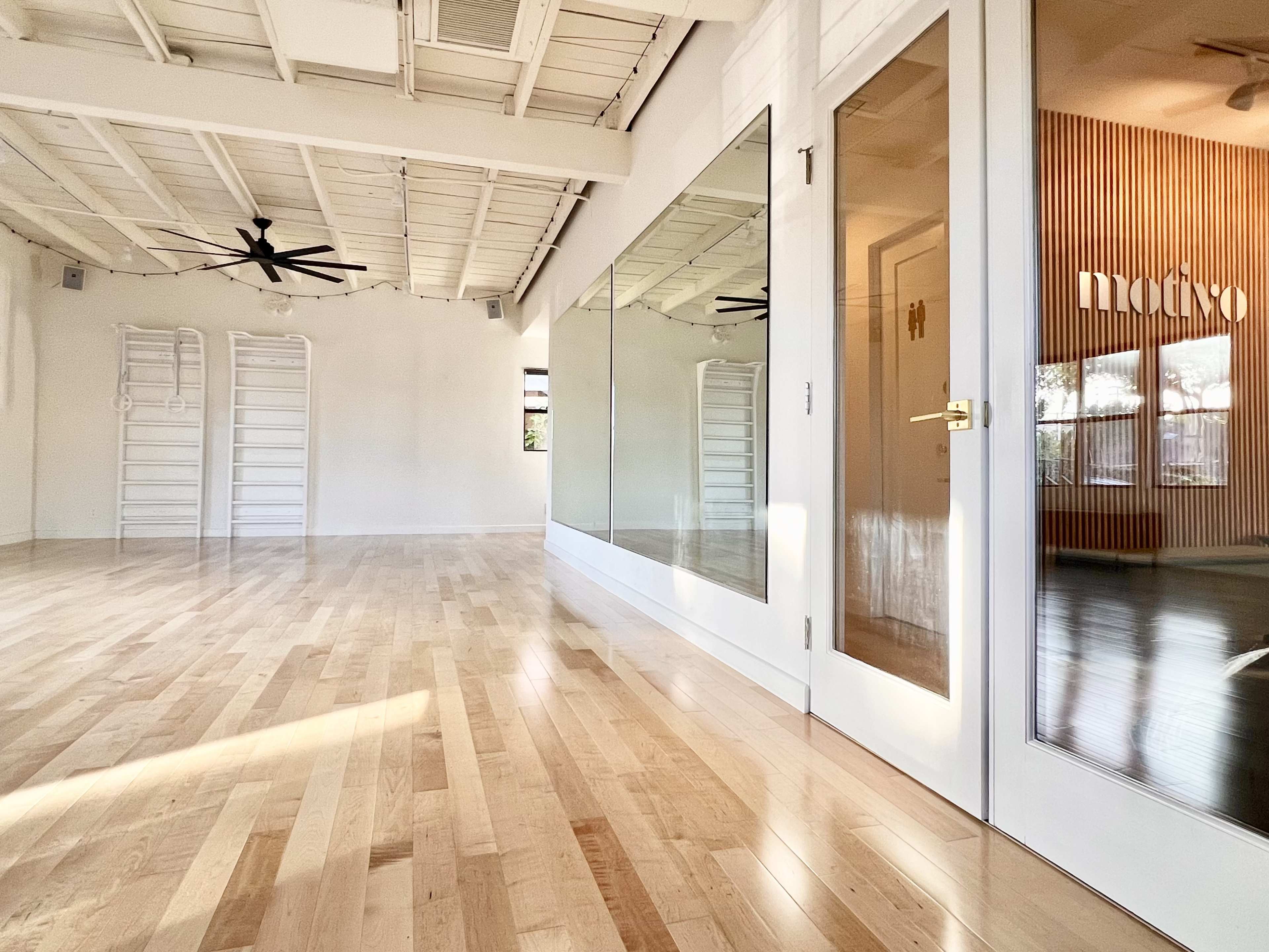 A bright, spacious interior with wooden floors, large mirrors, and glass doors leading to a well-lit room.