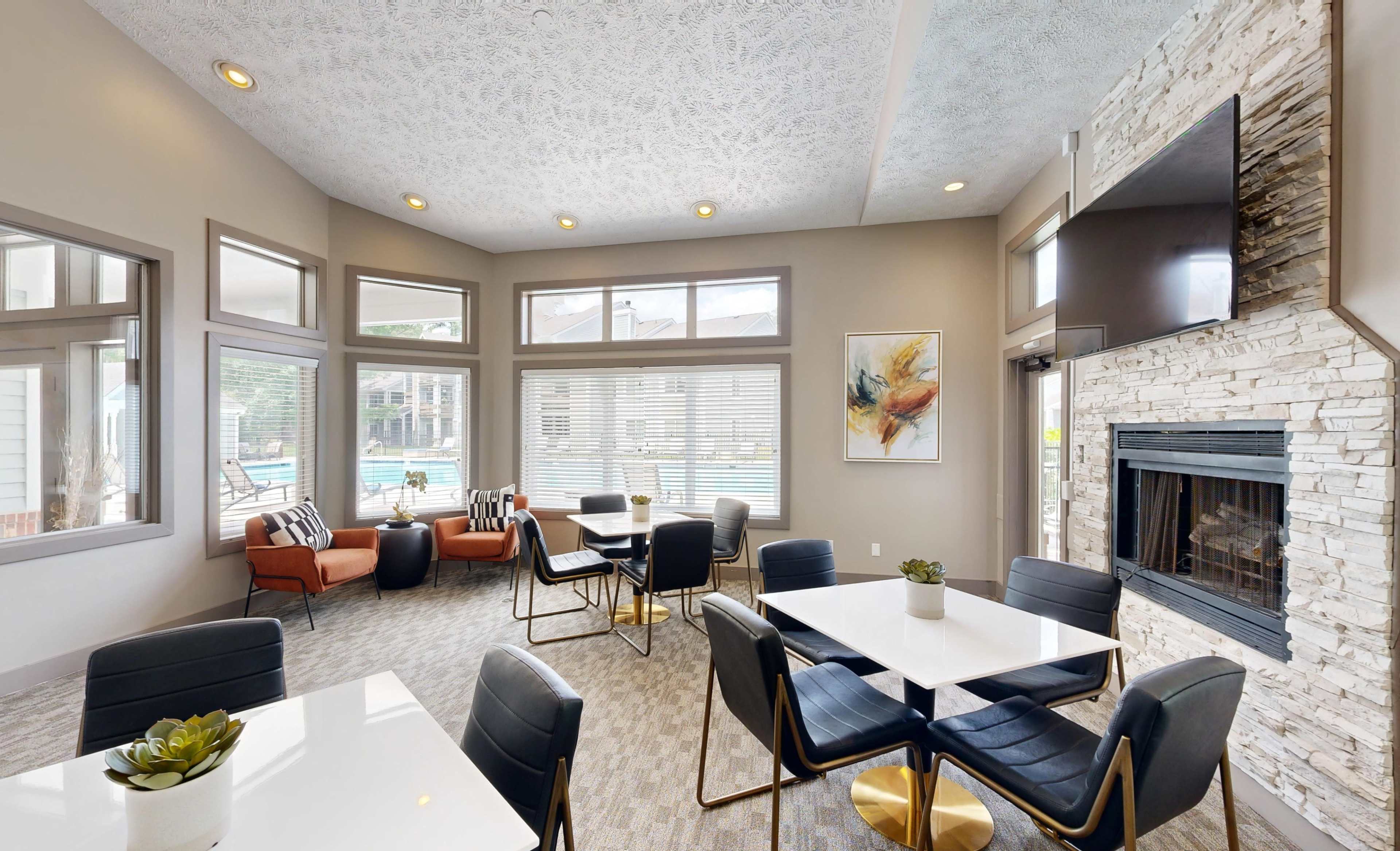 A modern lounge area features black and gold furniture, large windows, and a stone fireplace, overlooking an outdoor pool.