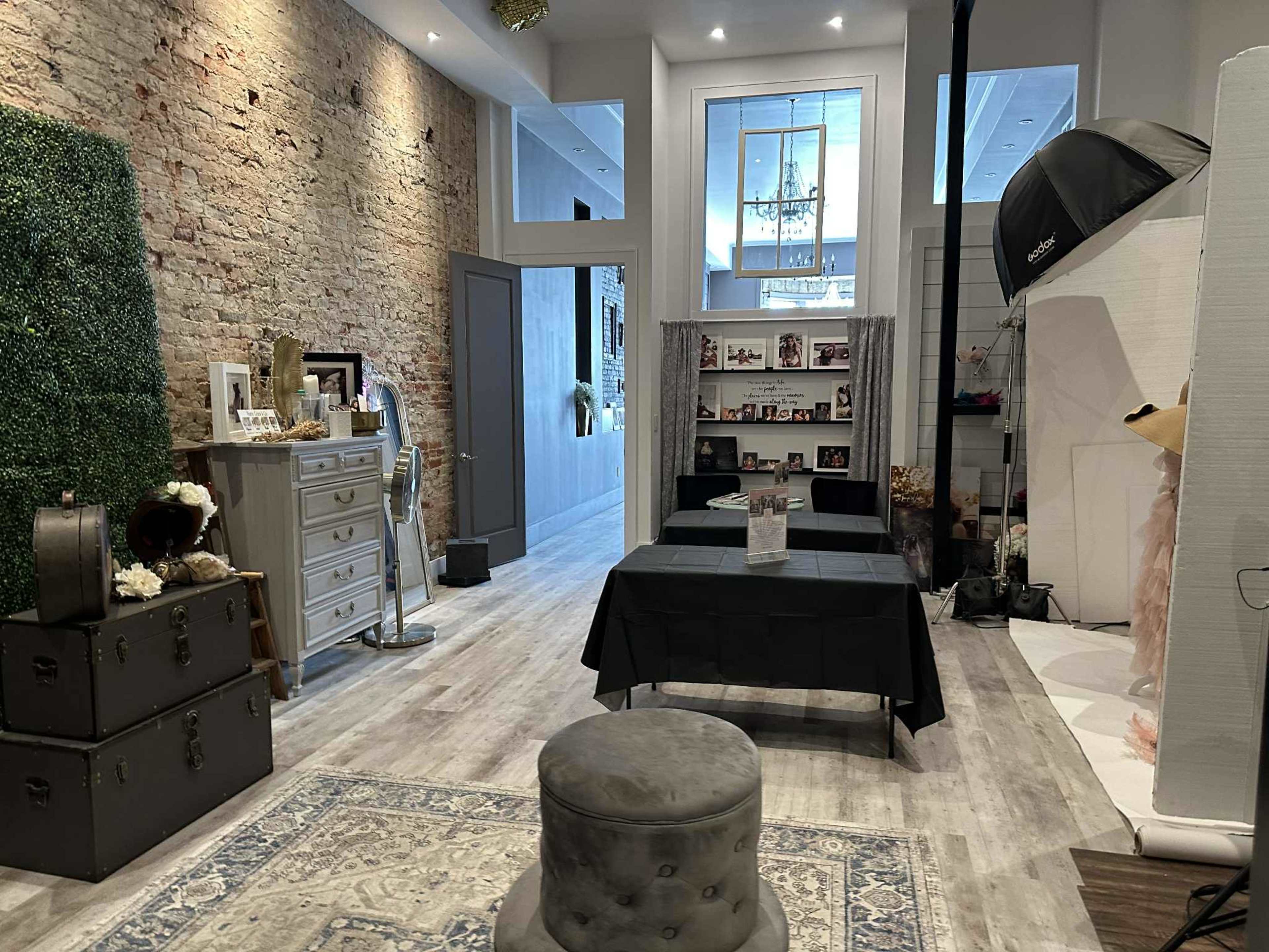 The image shows an interior space featuring a brick wall, a decorative green wall, a display of furniture, a table with a black cloth, and several shelves with framed photos.