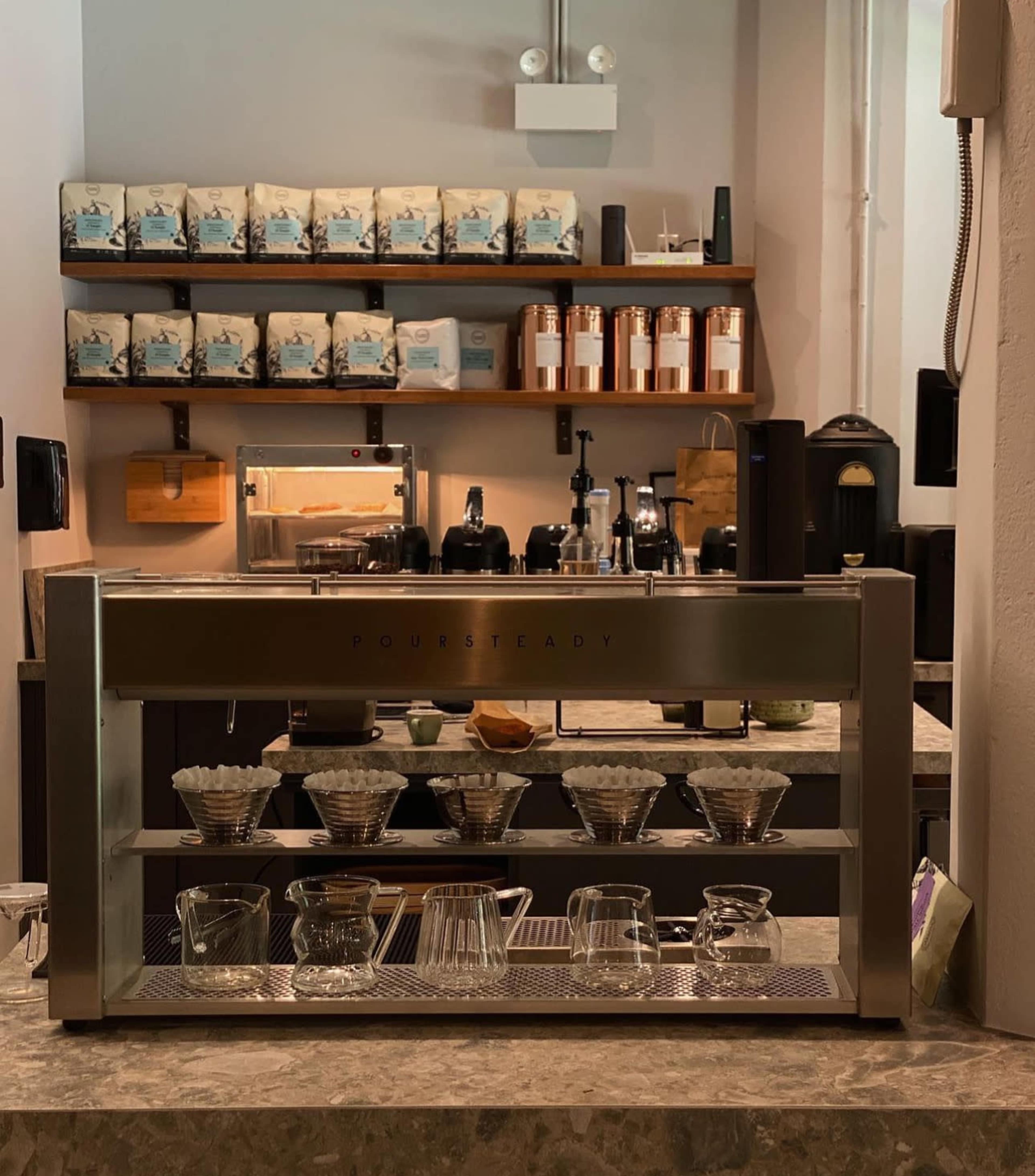 A coffee preparation station with brewing equipment and neatly arranged coffee bags on shelves in the background.