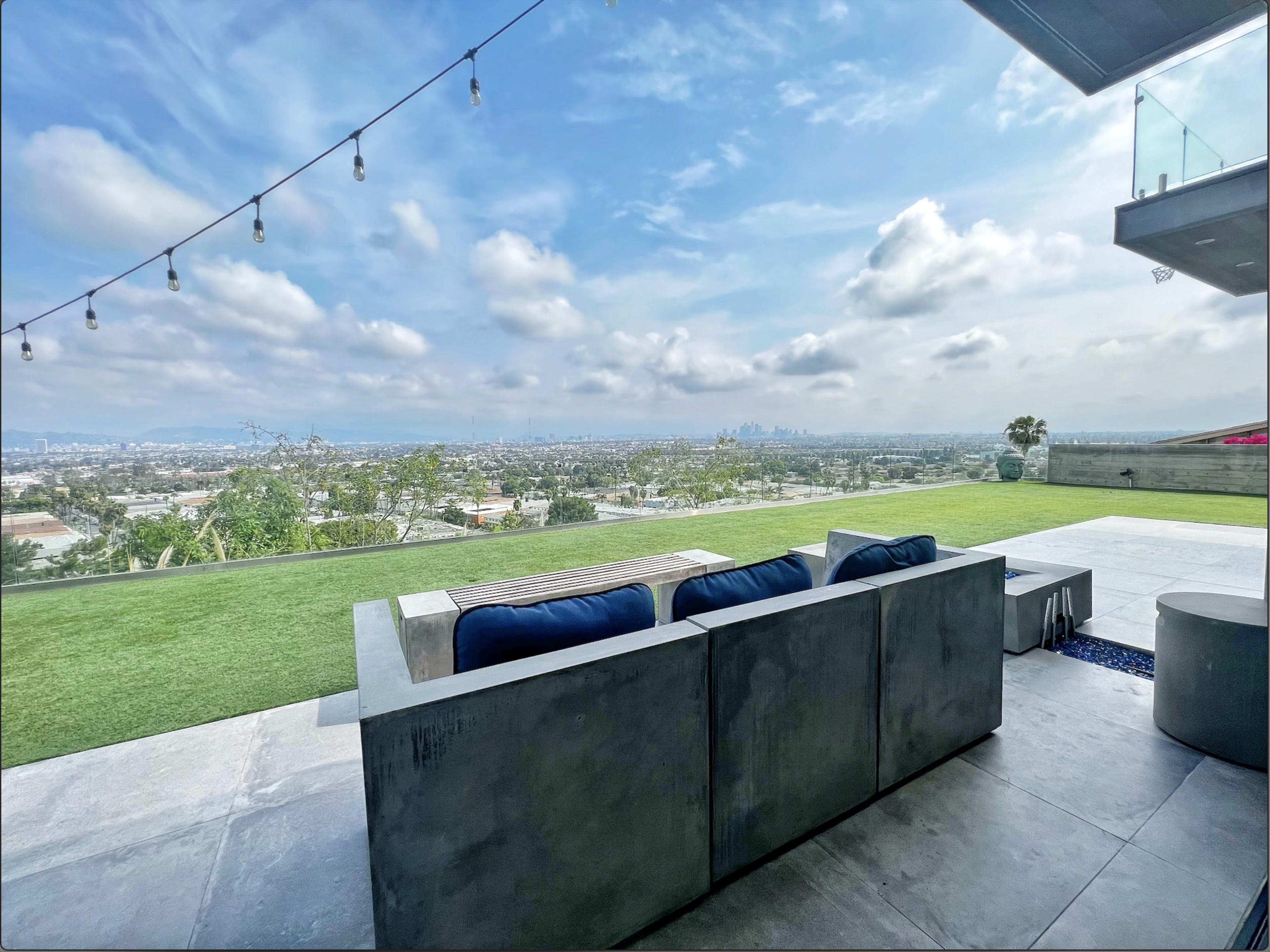A modern outdoor seating area with concrete furniture overlooks a sprawling city landscape under a cloudy sky.
