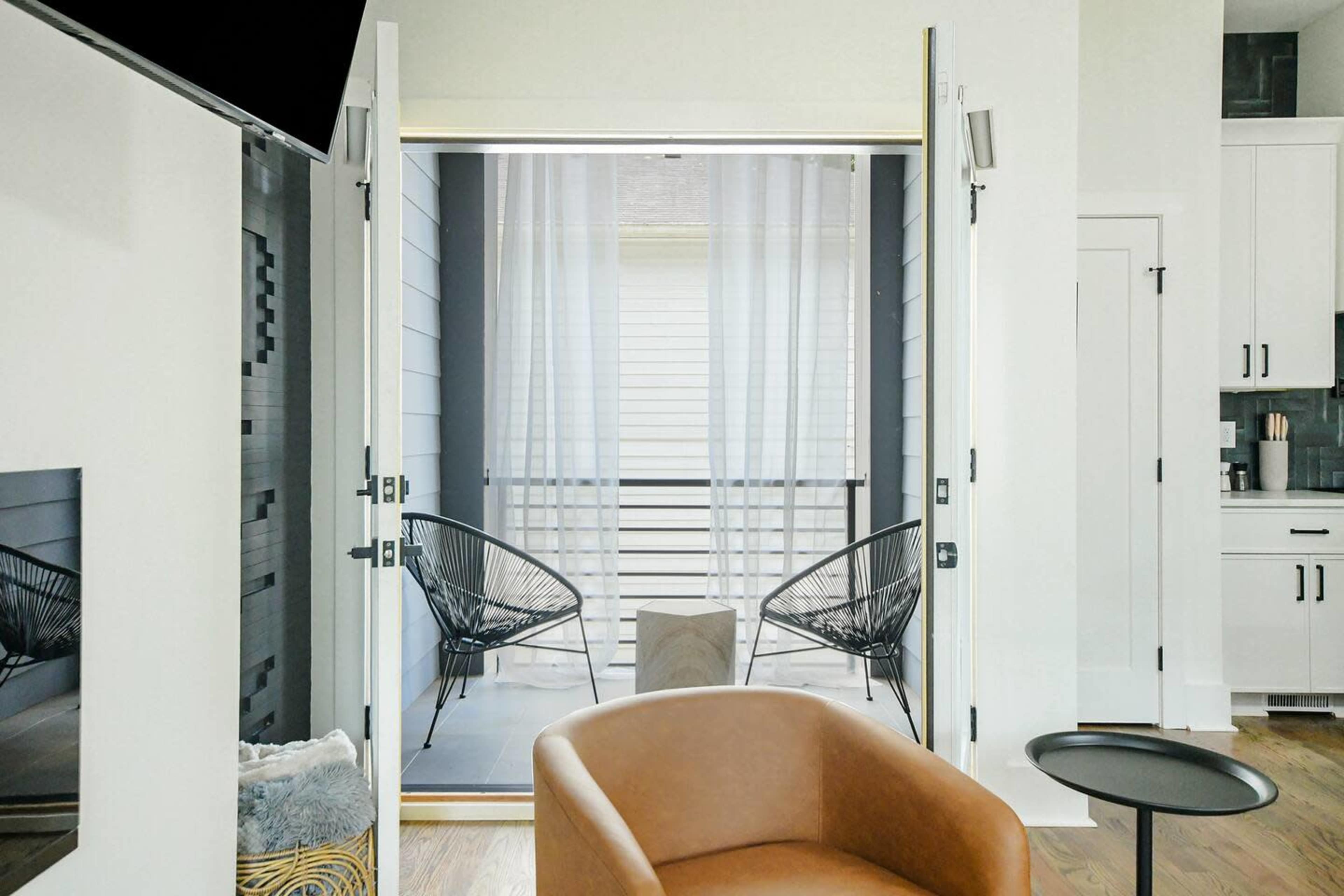 The image shows an interior space with an open doorway leading to a small balcony area, featuring two chairs and a small table.