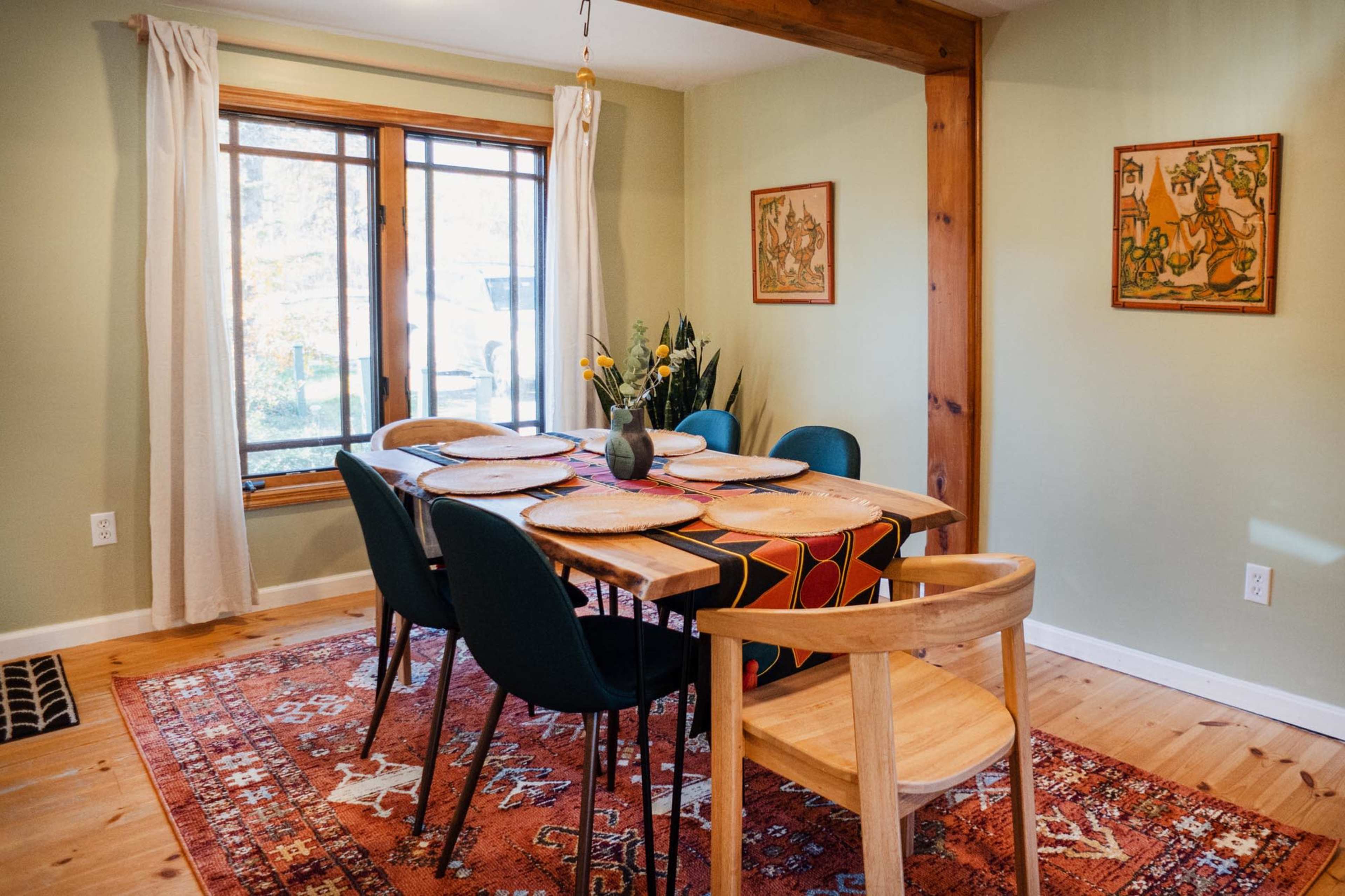 The dining room features a wooden table set with placemats, surrounded by green chairs, and a large window allowing natural light.