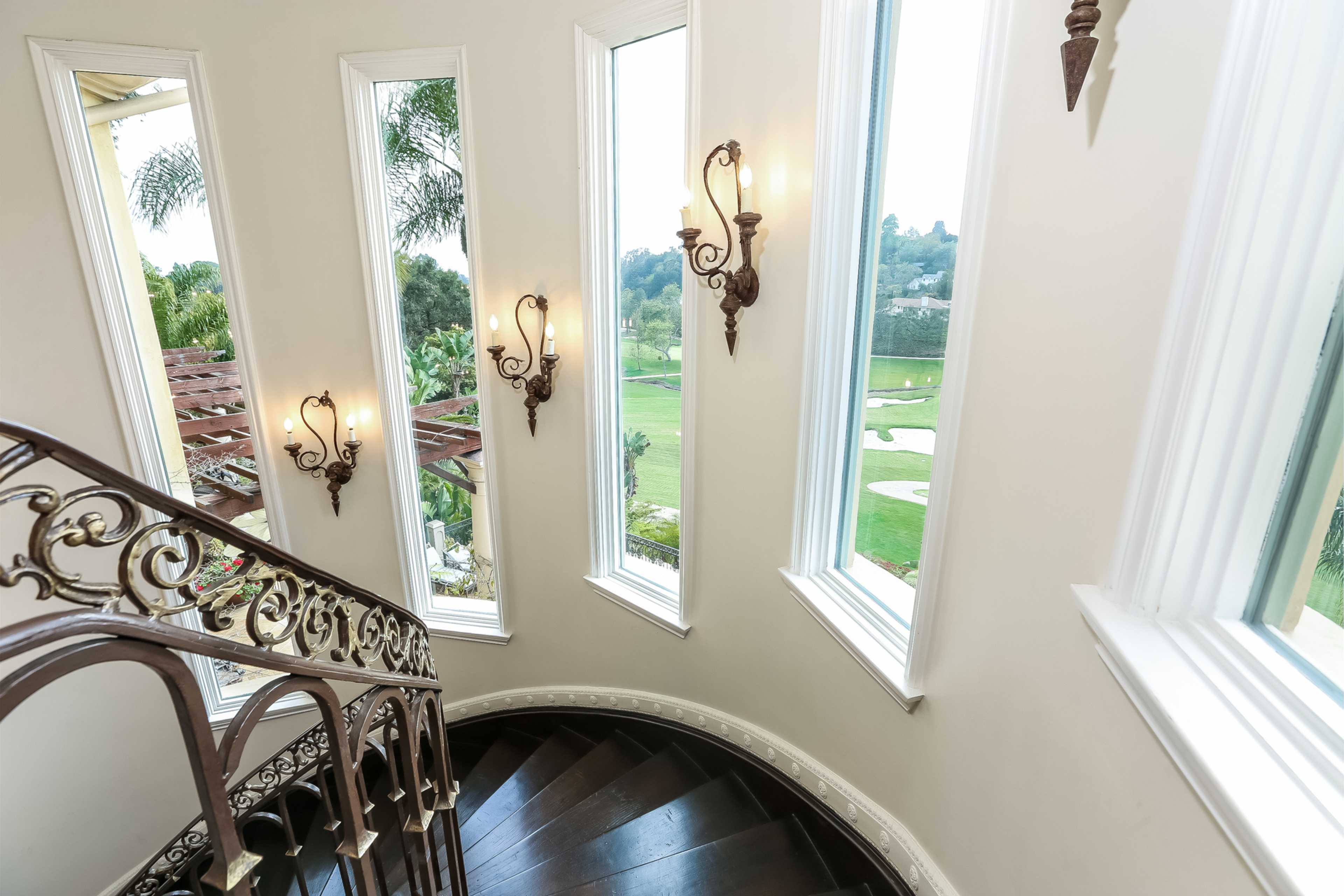 A spiral staircase descends alongside large windows with views of a green landscape and golf course.