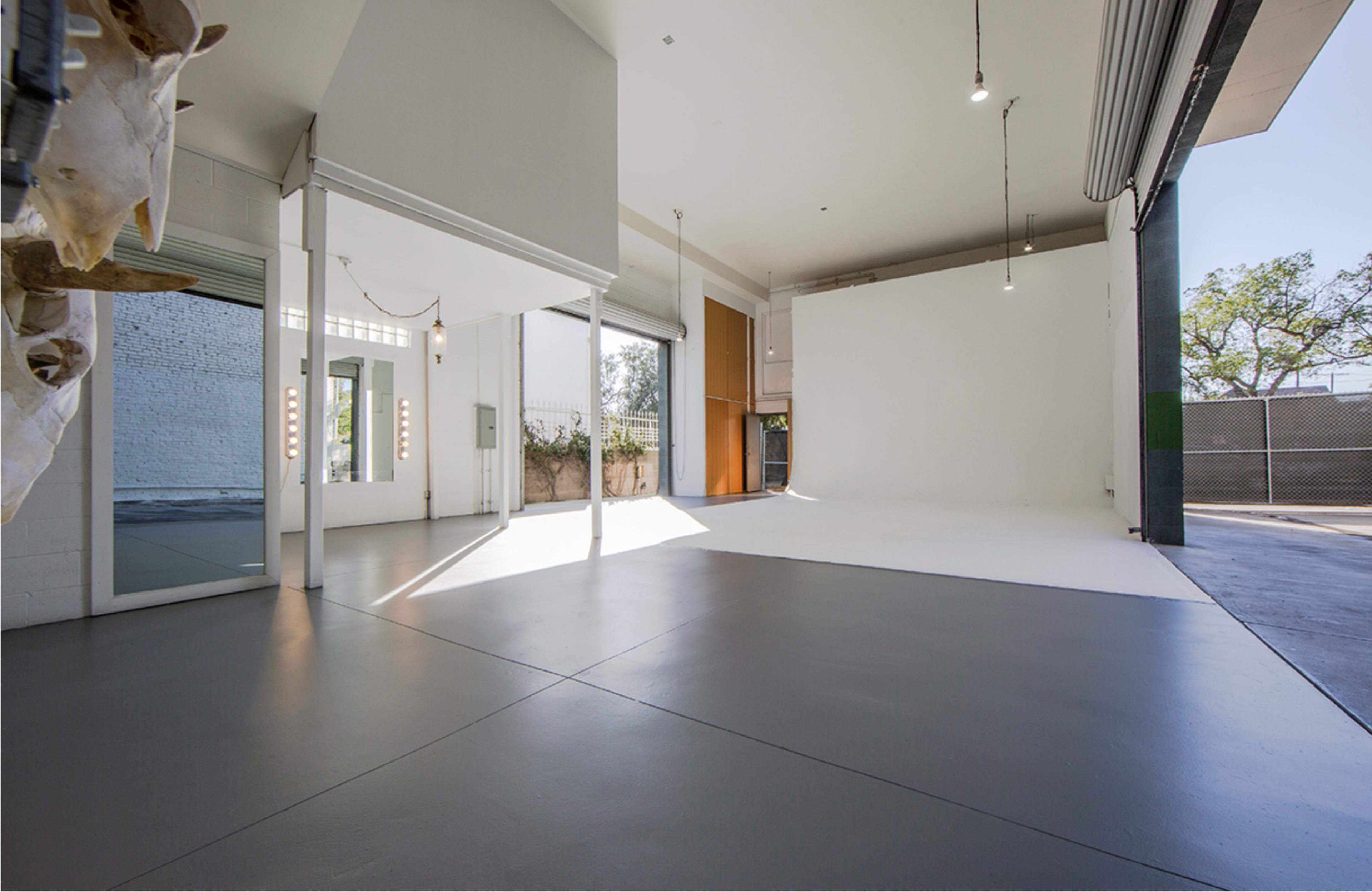 A spacious, empty studio with white walls, large windows, and a gray floor.