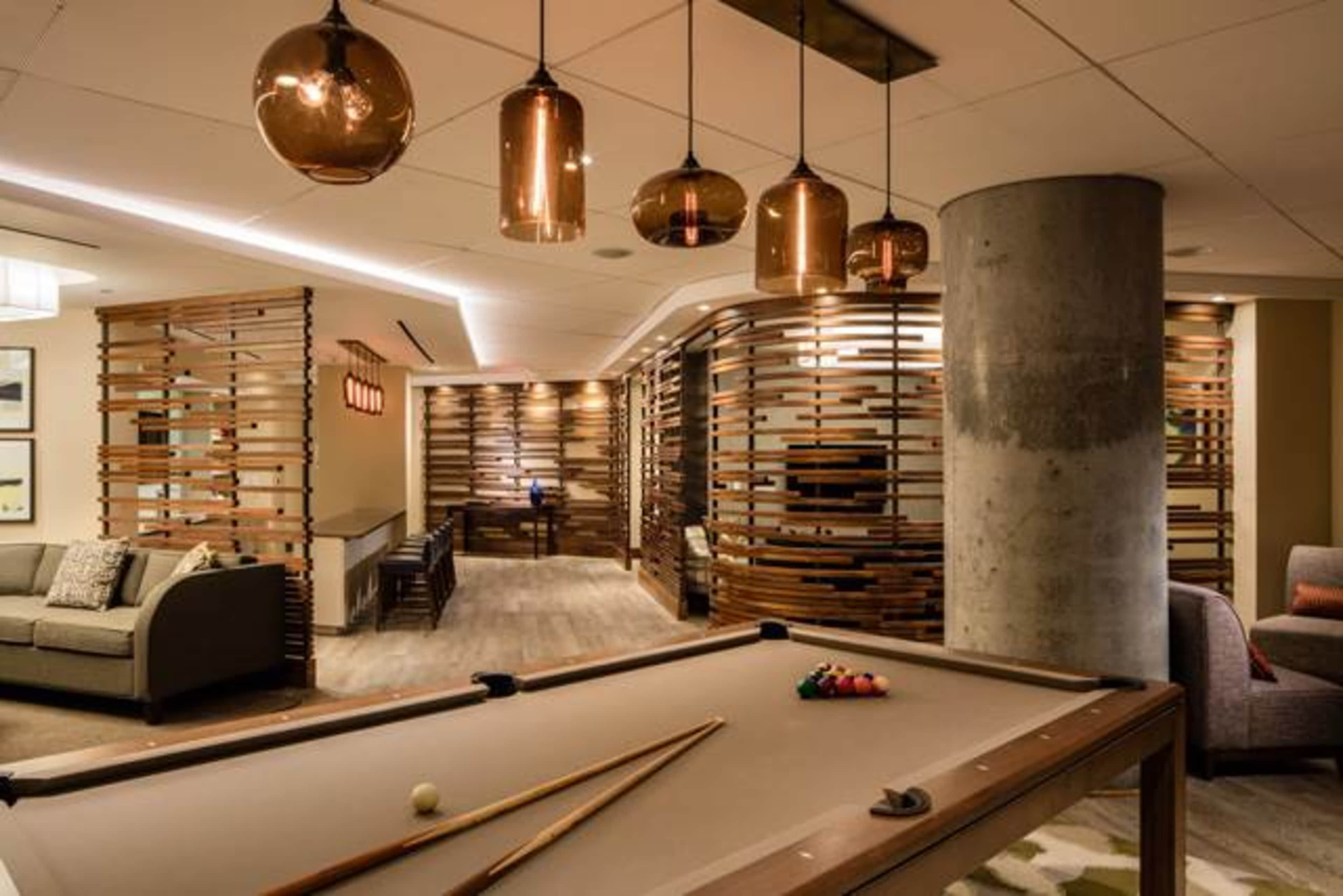 A modern recreation room with a billiards table in the foreground and stylish pendant lights hanging from the ceiling.