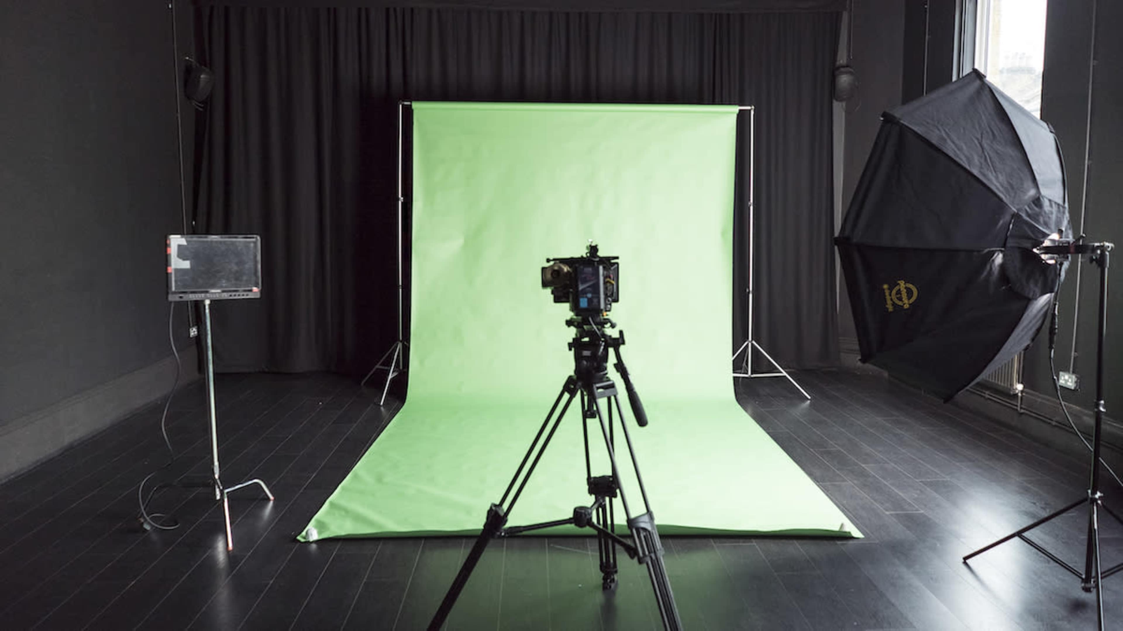 A photography studio is set up with a green backdrop, a camera on a tripod, and softbox lighting.