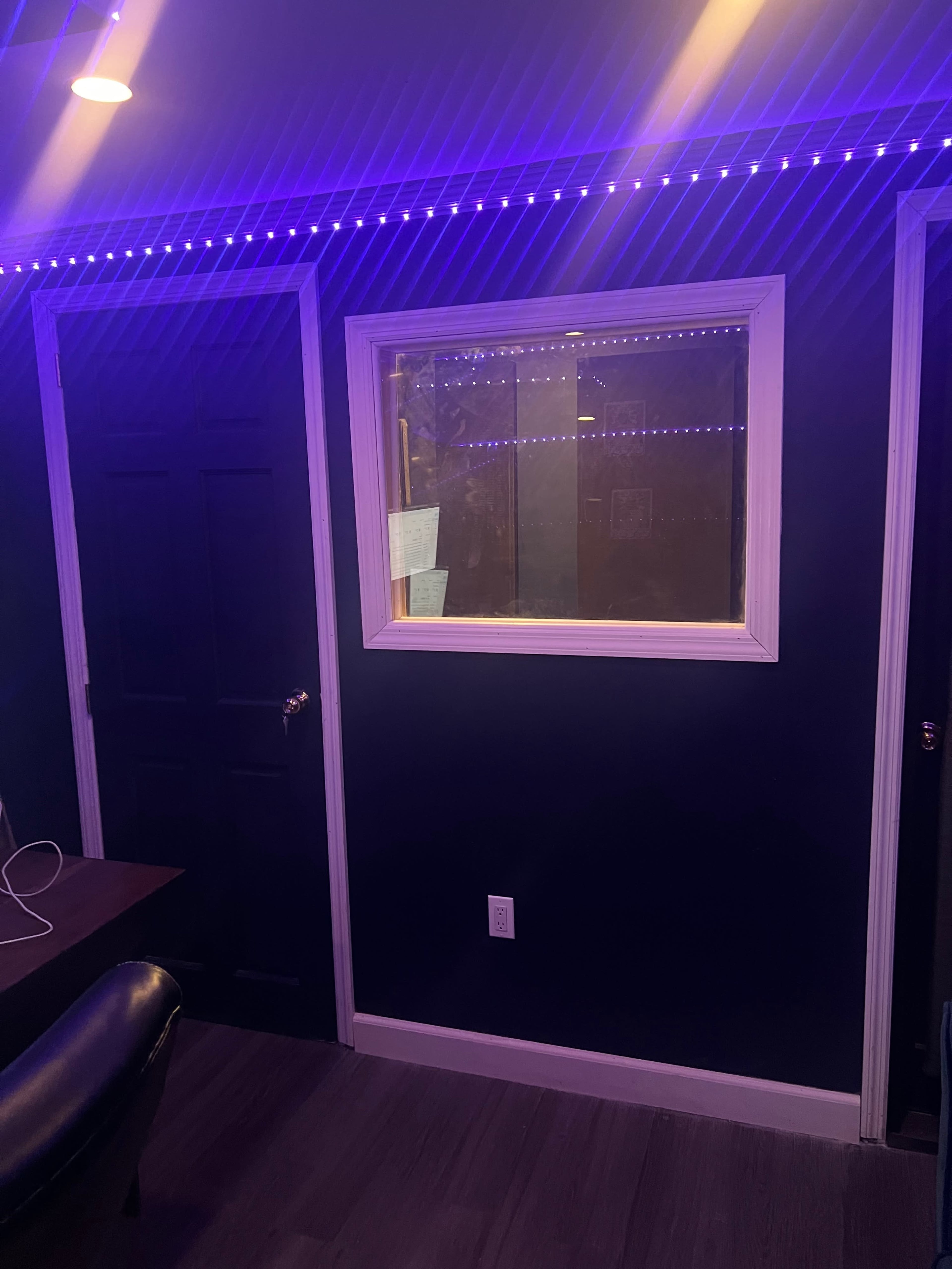 A dimly lit room with a window framed in white, blue LED lights along the top, and two doors.