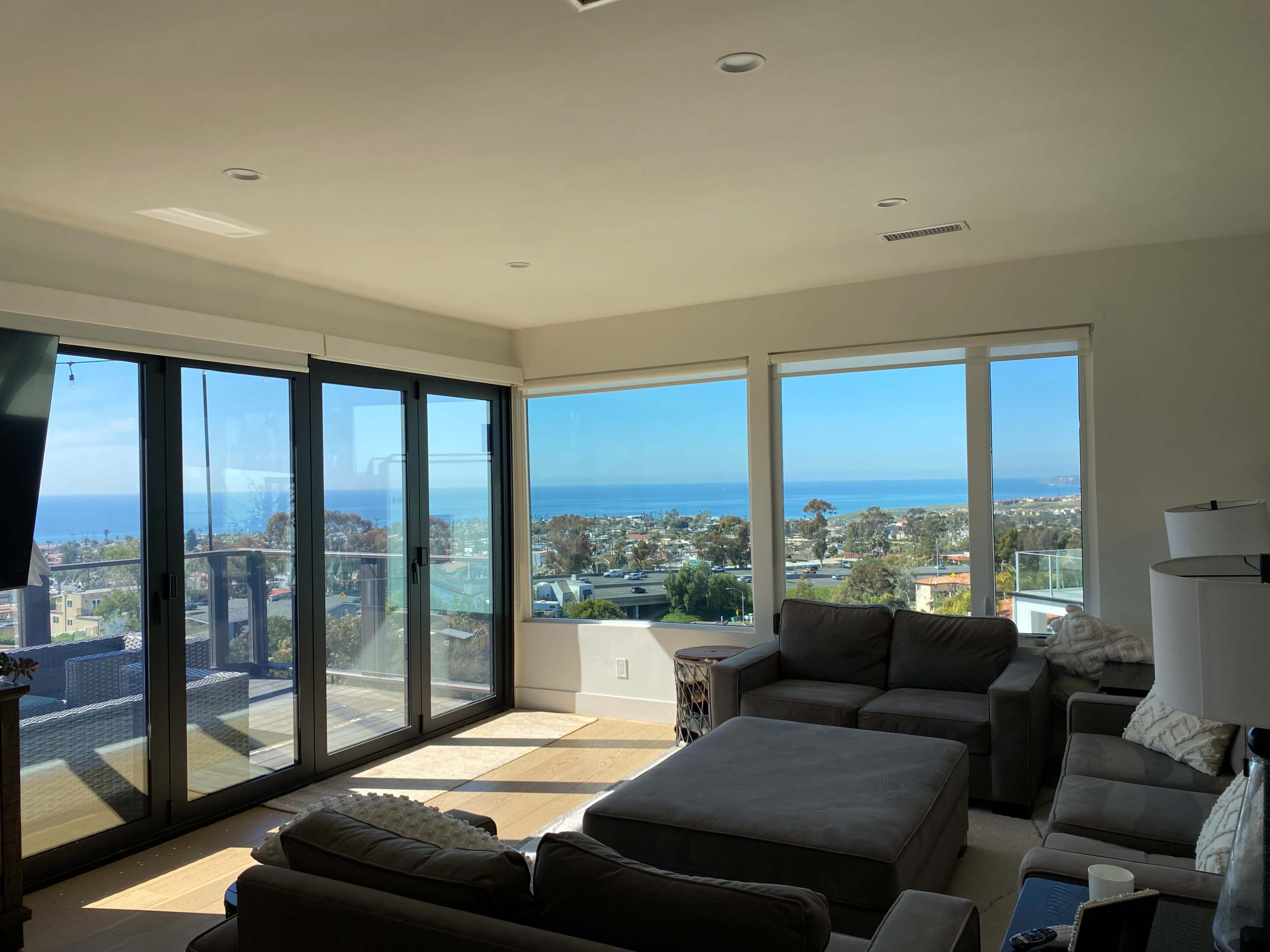 A spacious living room features large windows overlooking a coastal view with a seating area and a television setup.