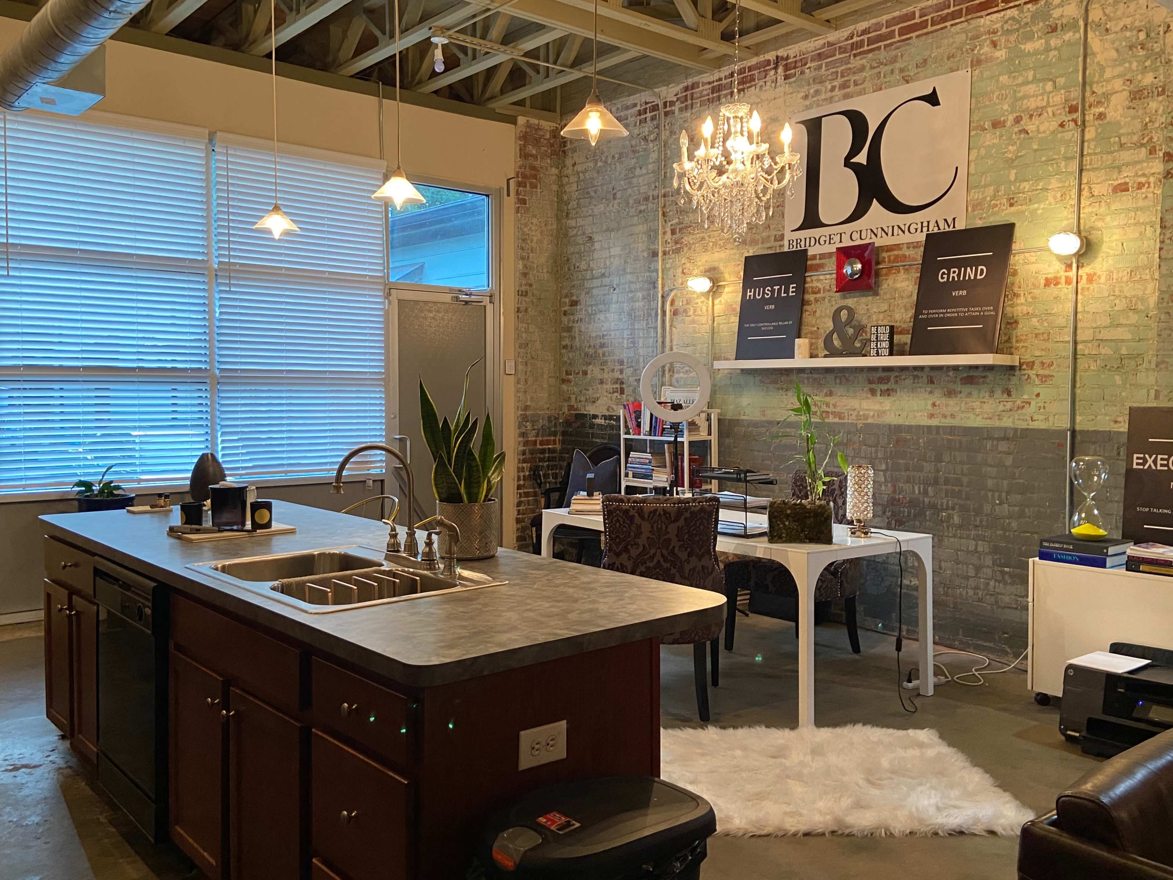 A modern office space with a kitchen island, a white desk set up for work, and industrial-style brick walls.