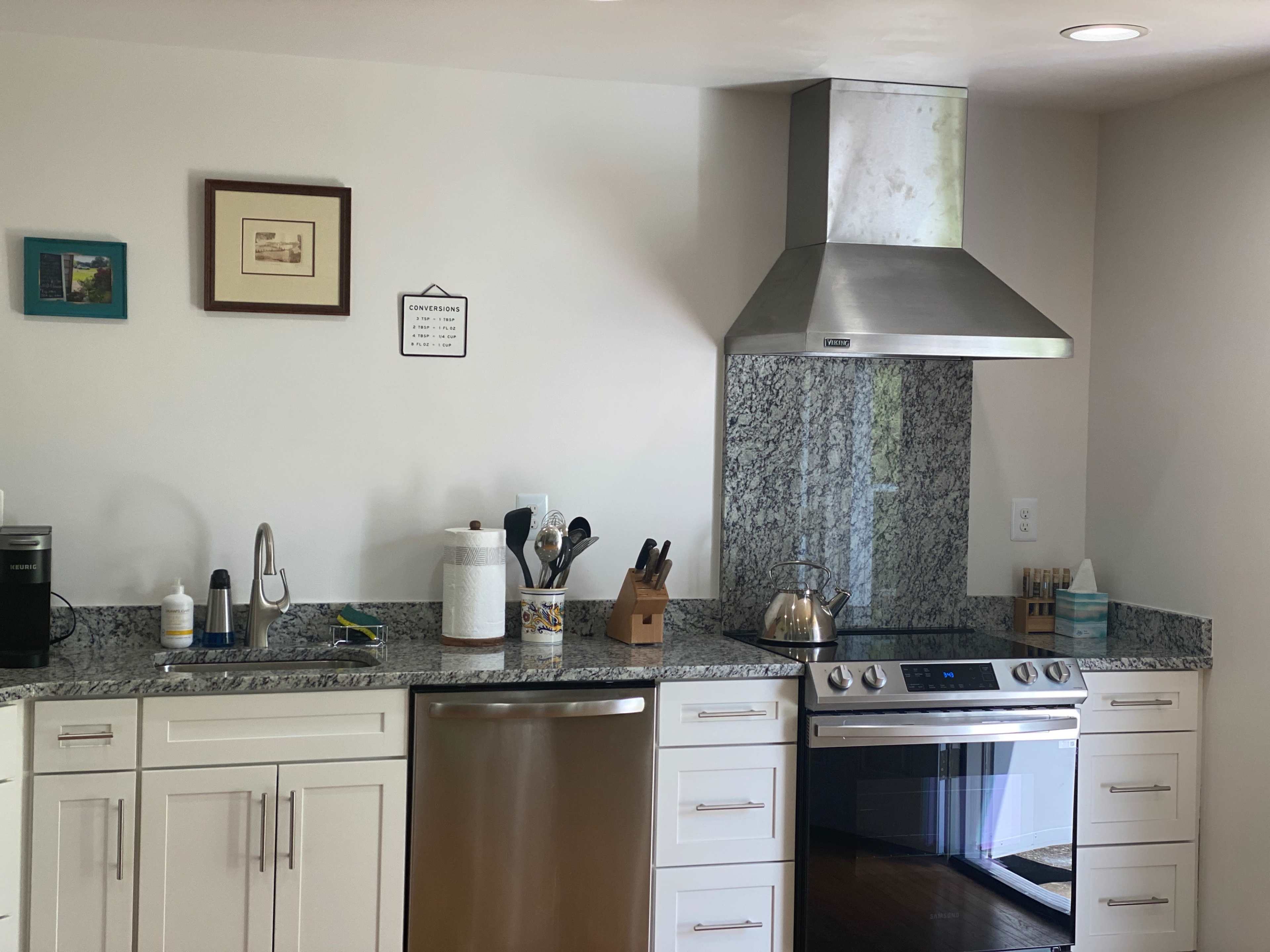 The image shows a modern kitchen with silver appliances, a granite countertop, and a stainless steel range hood above the stovetop.