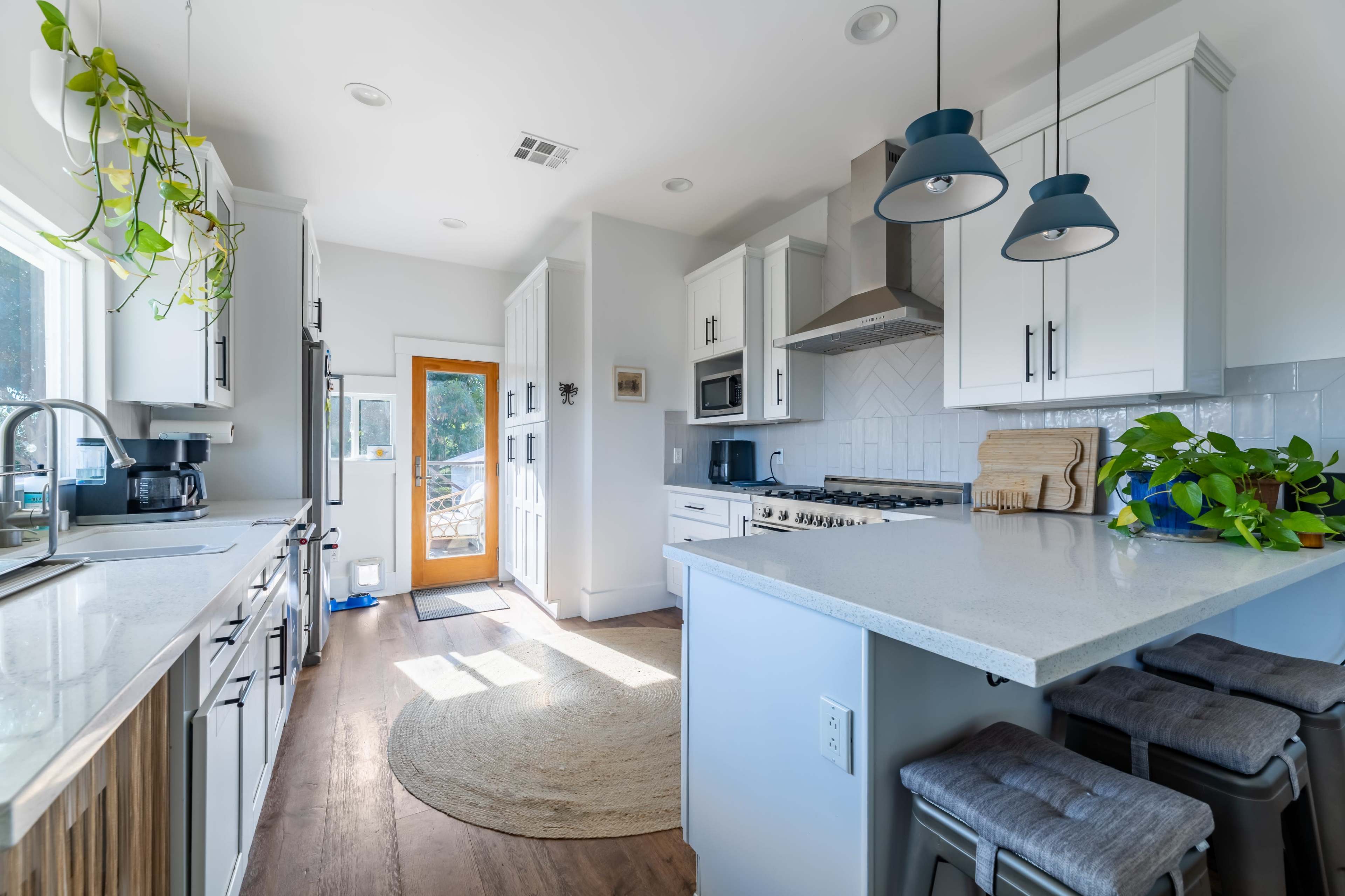 The kitchen features white cabinetry, stainless steel appliances, a round rug, and a door leading to an outdoor area.