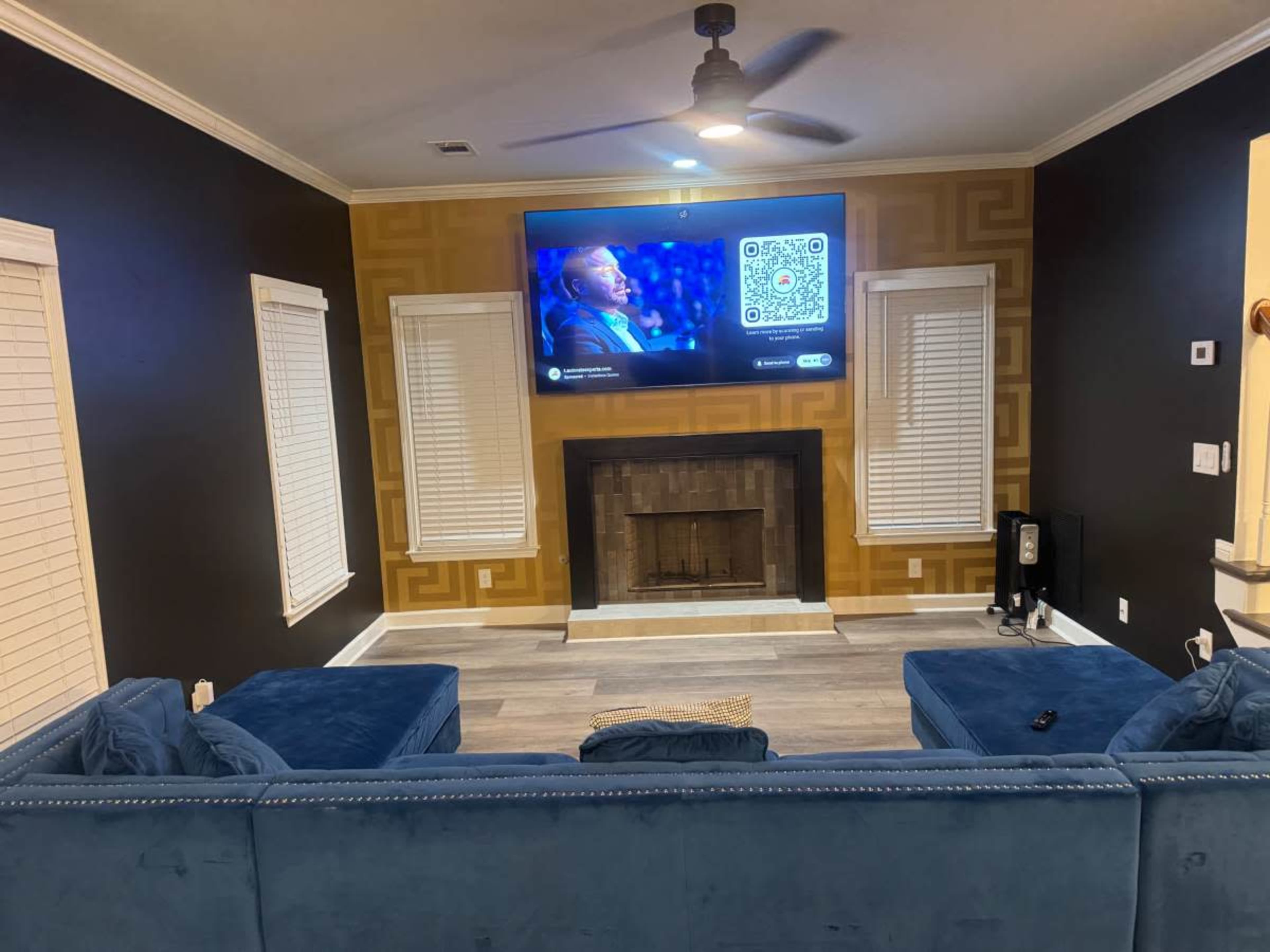 The living room features a blue sectional sofa, a television mounted on the wall, and a fireplace with a wooden mantel.