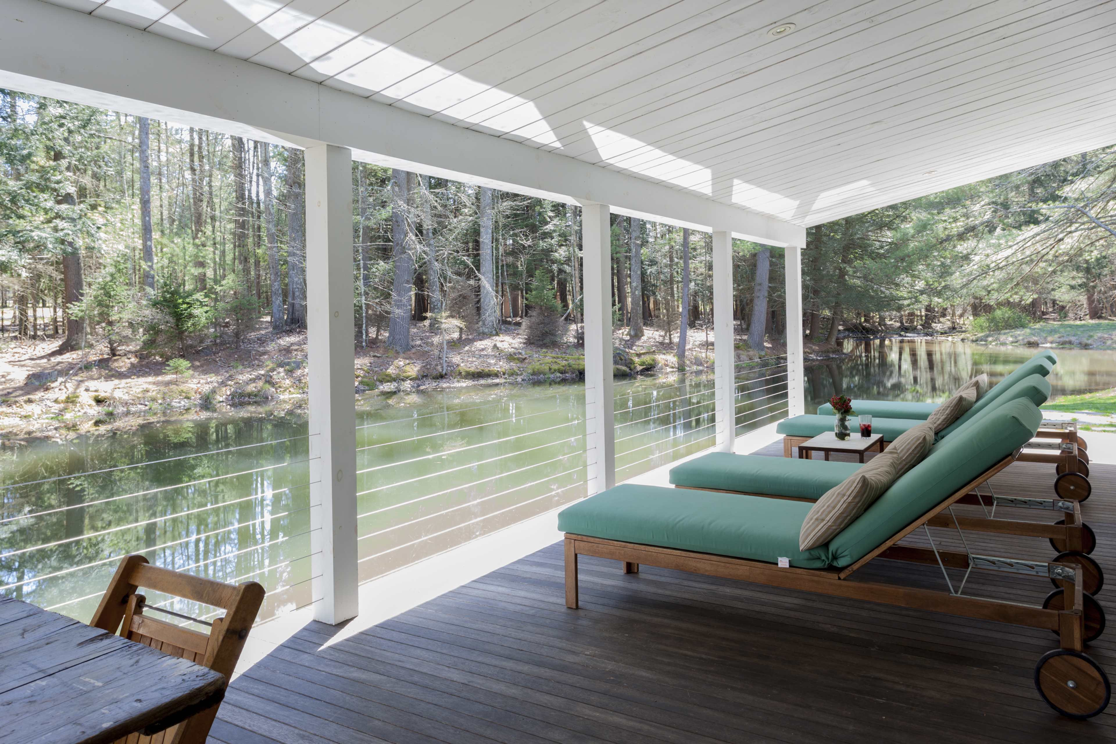 A deck with green lounge chairs overlooks a calm river surrounded by trees.