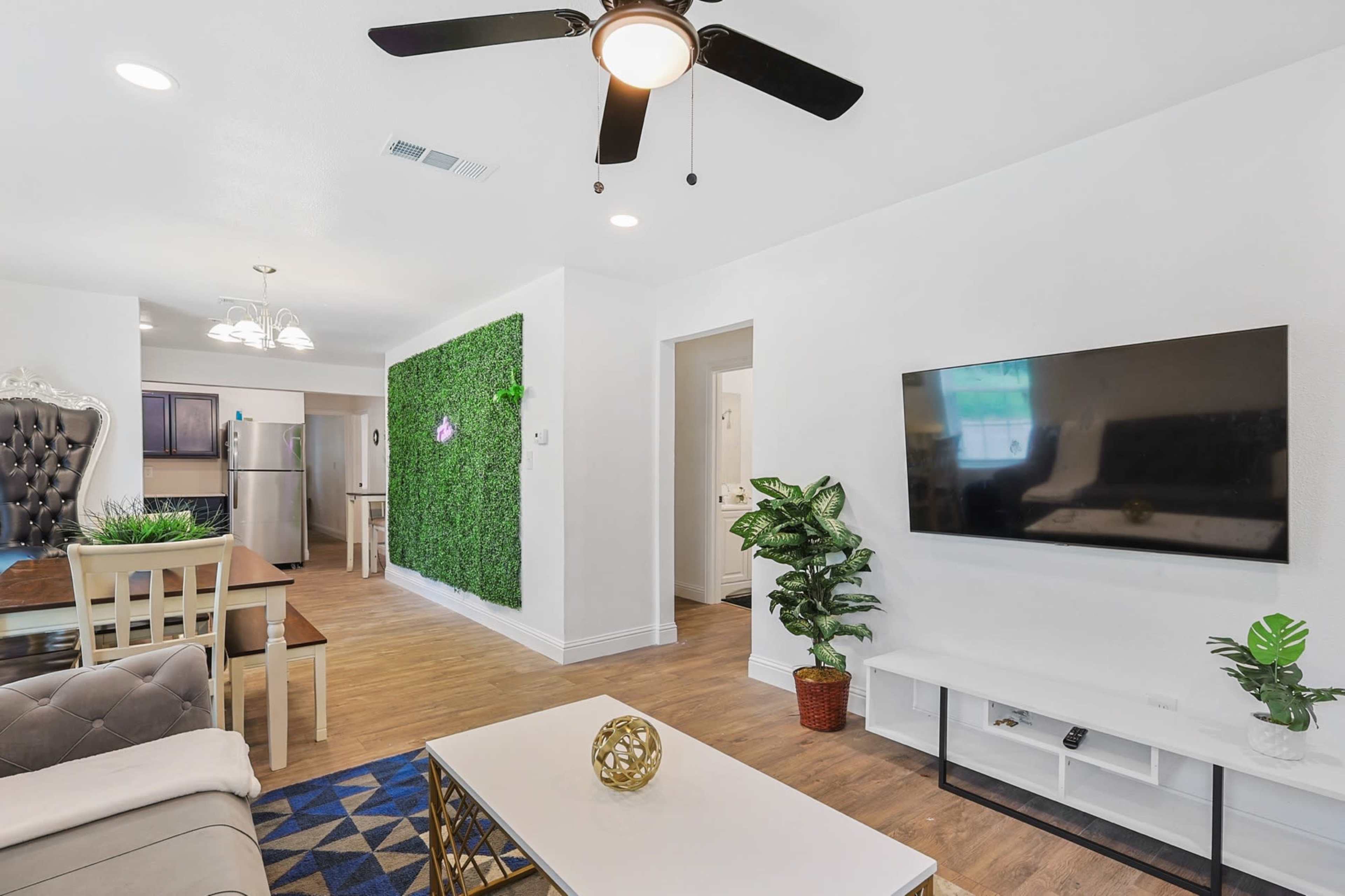 A modern living room with a stylish couch, a television mounted on the wall, and a green accent wall made of artificial plants.