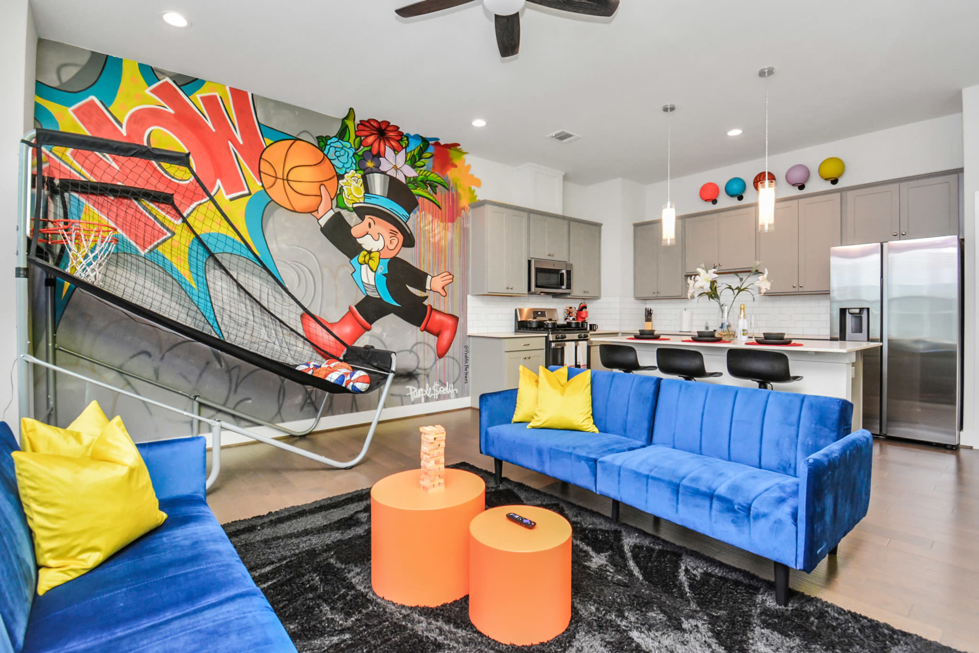 A modern living area with blue couches, a basketball hoop integrated into the wall, and a colorful mural featuring a character playing basketball.