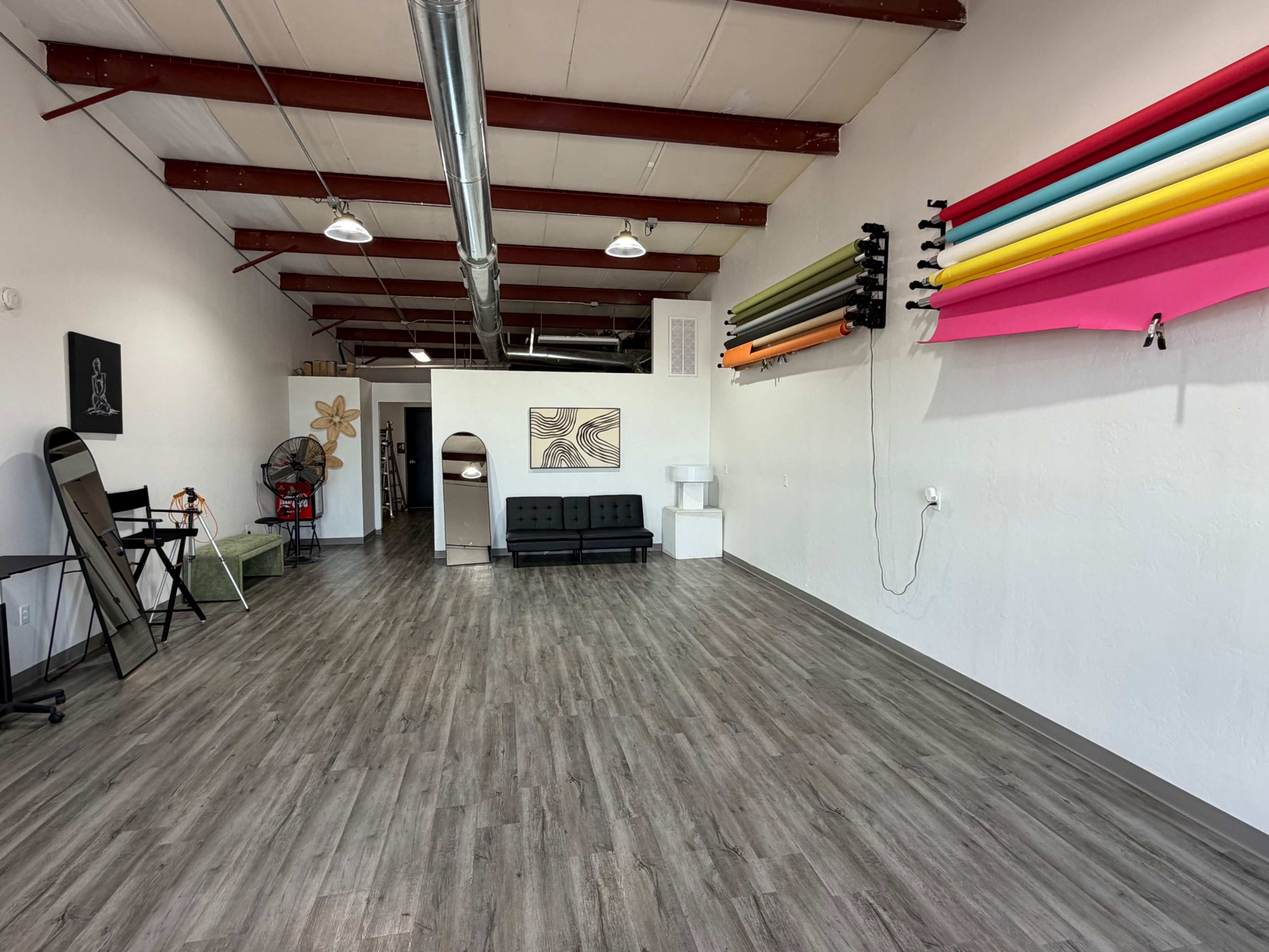 The image shows a spacious, well-lit interior with a seating area, colorful backdrops on the wall, and minimal furnishings.