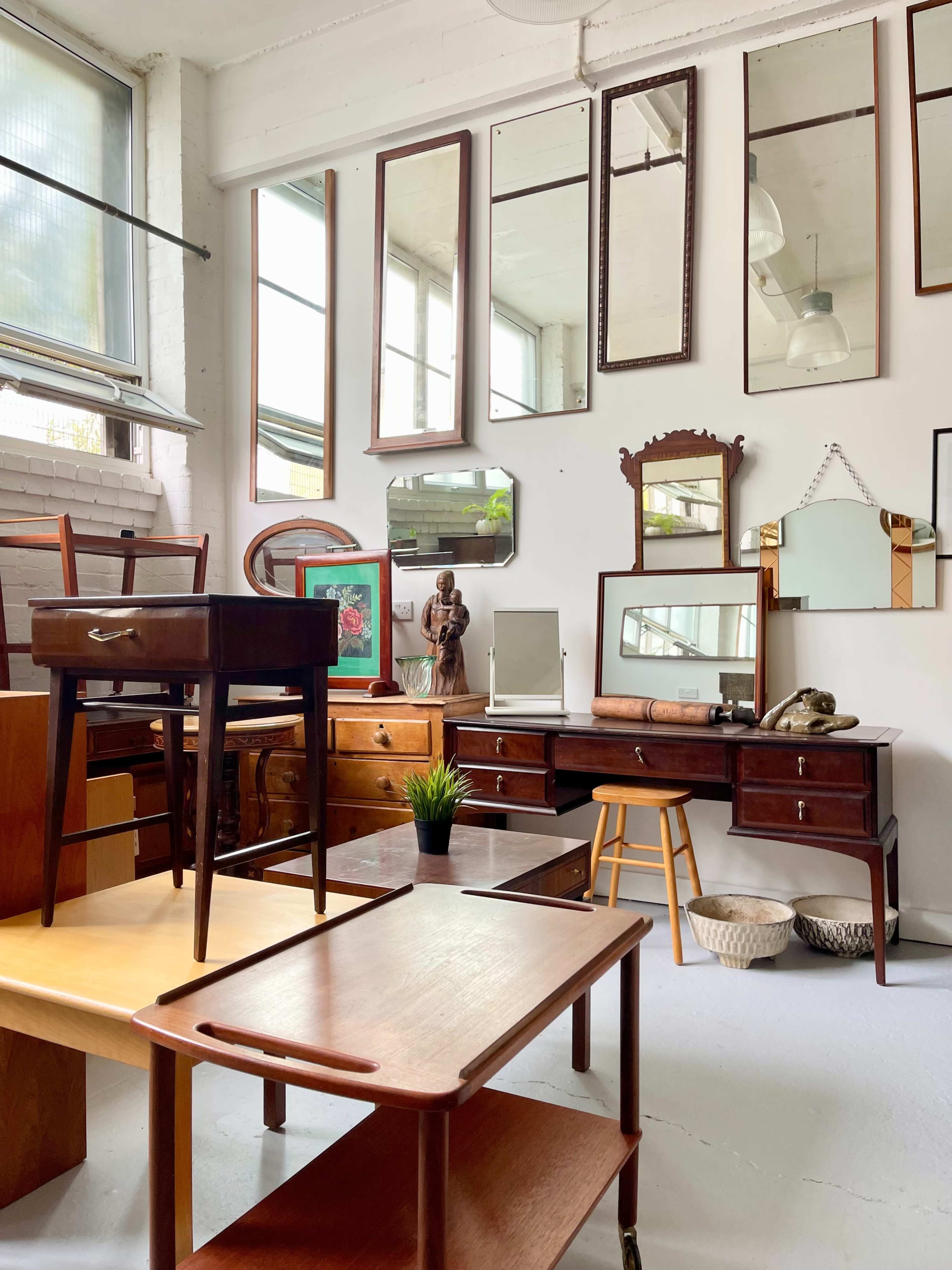A room filled with various wooden furniture pieces, including tables, chairs, and mirrors, arranged amidst a bright and airy interior.