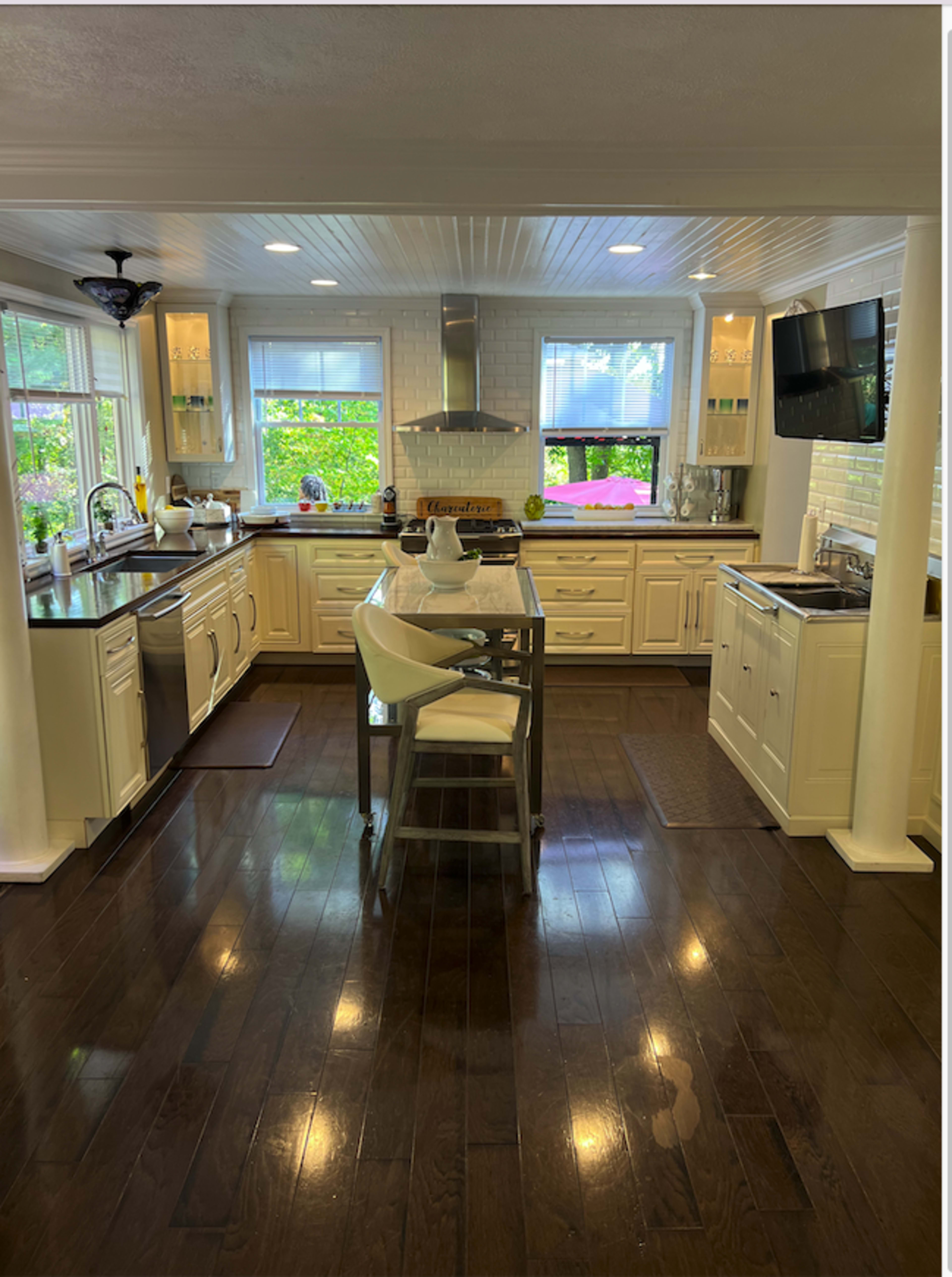 A modern kitchen features an island with seating, stainless steel appliances, white cabinetry, and large windows providing natural light.