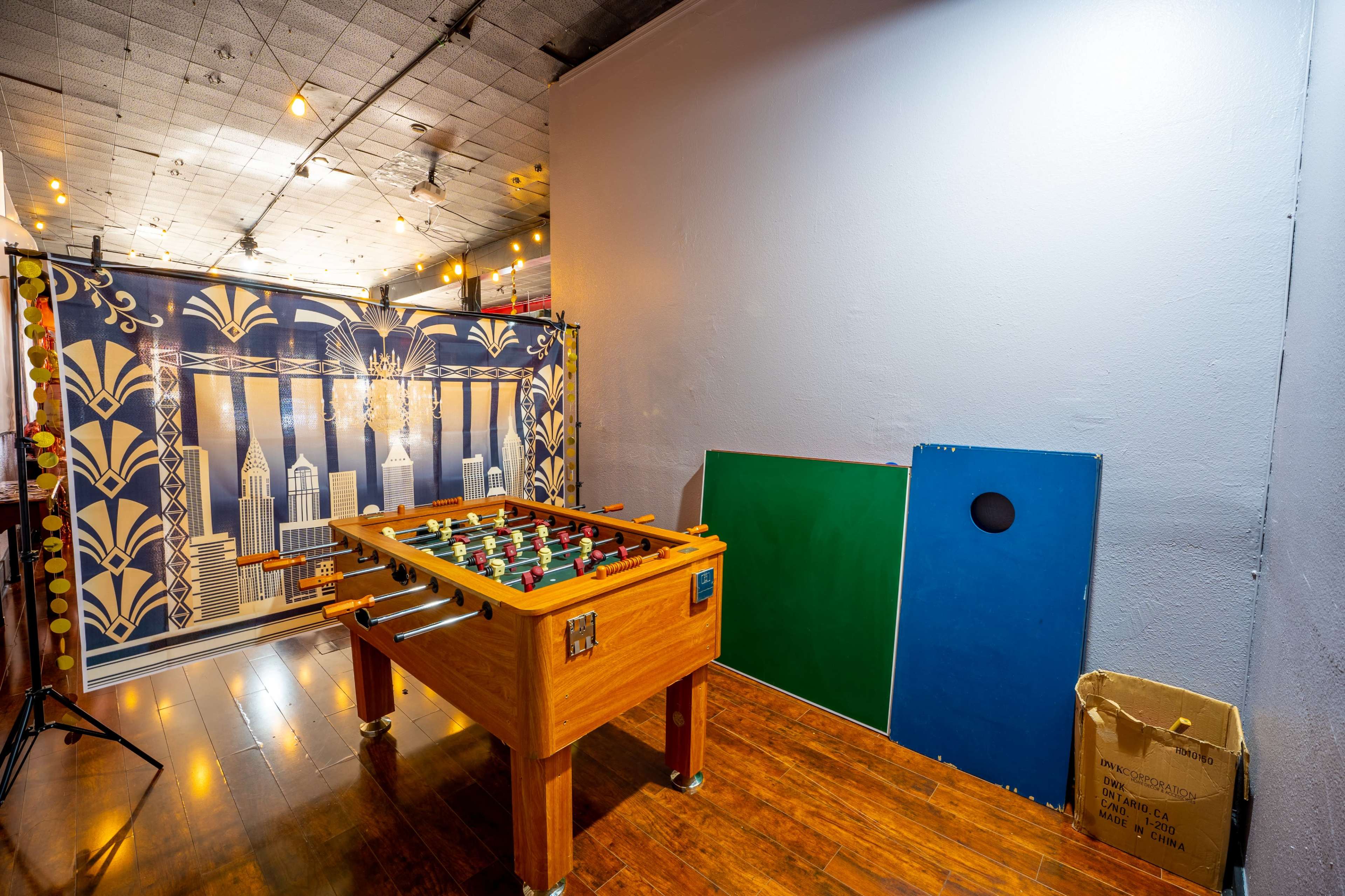 A foosball table in front of a decorative backdrop featuring a city skyline, with a plain wall and colored panels nearby.