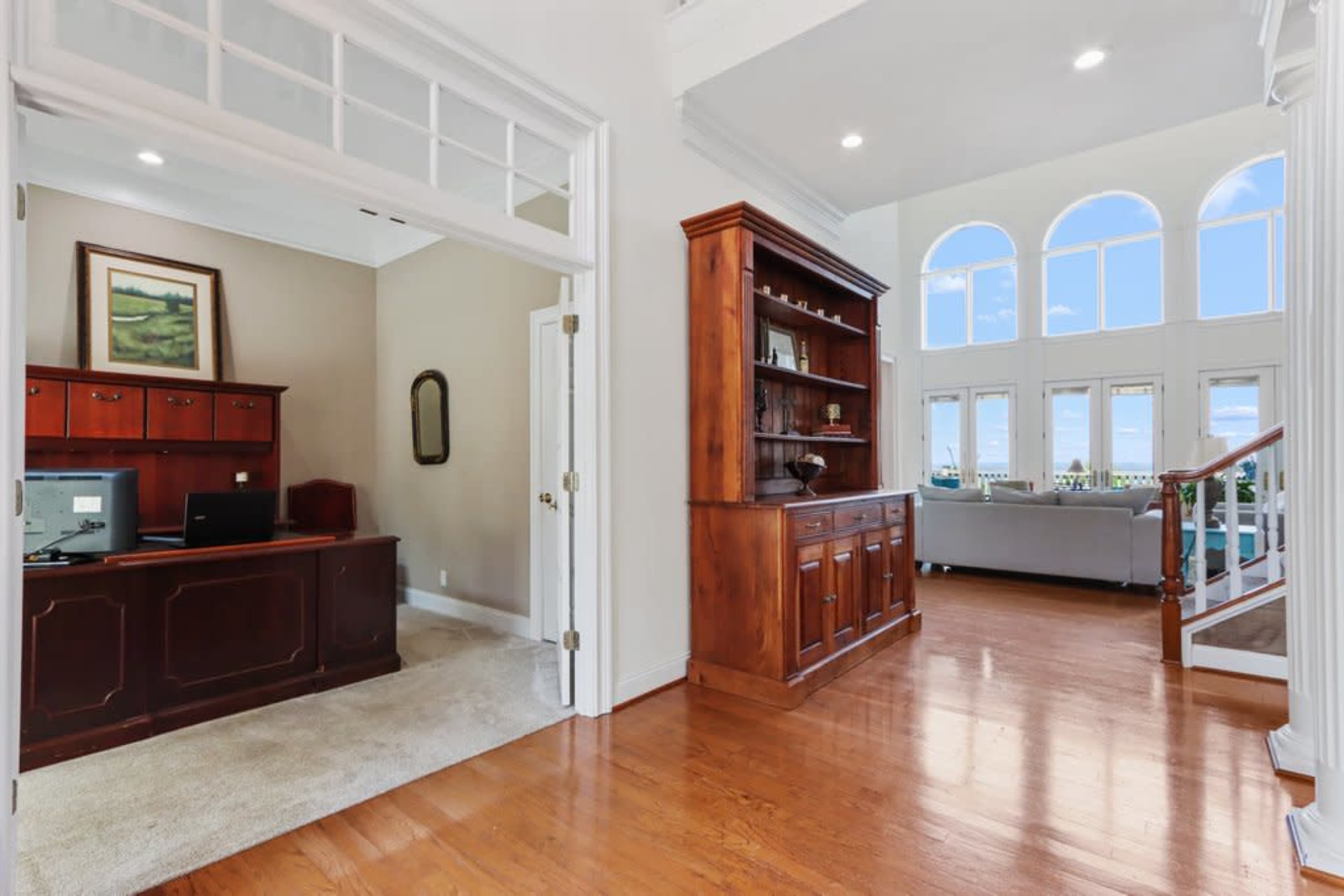 A spacious entryway leading to a home office with a desk and a living area featuring large windows.