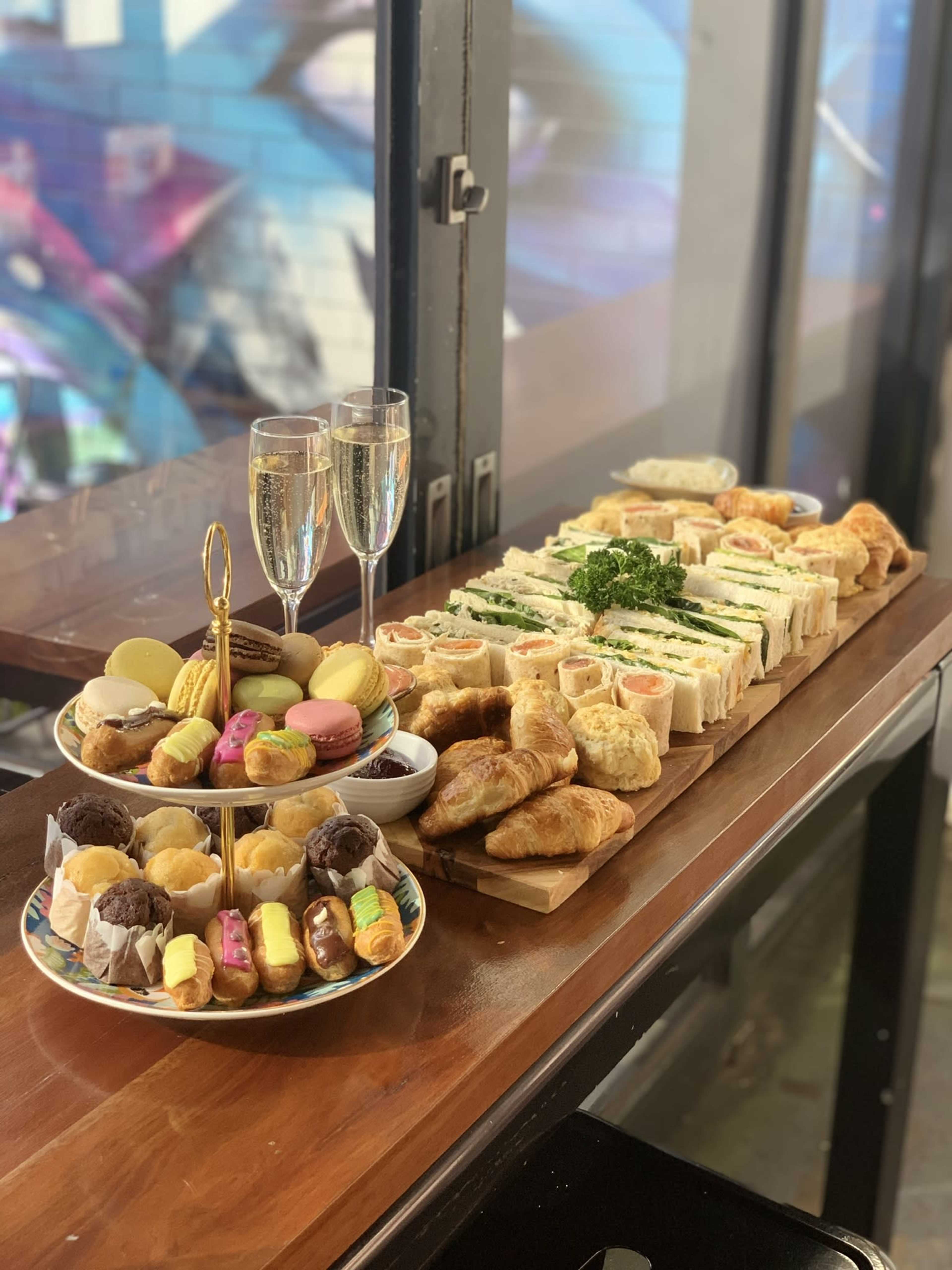 A table displaying an assortment of sandwiches, pastries, and desserts, accompanied by two glasses of champagne.