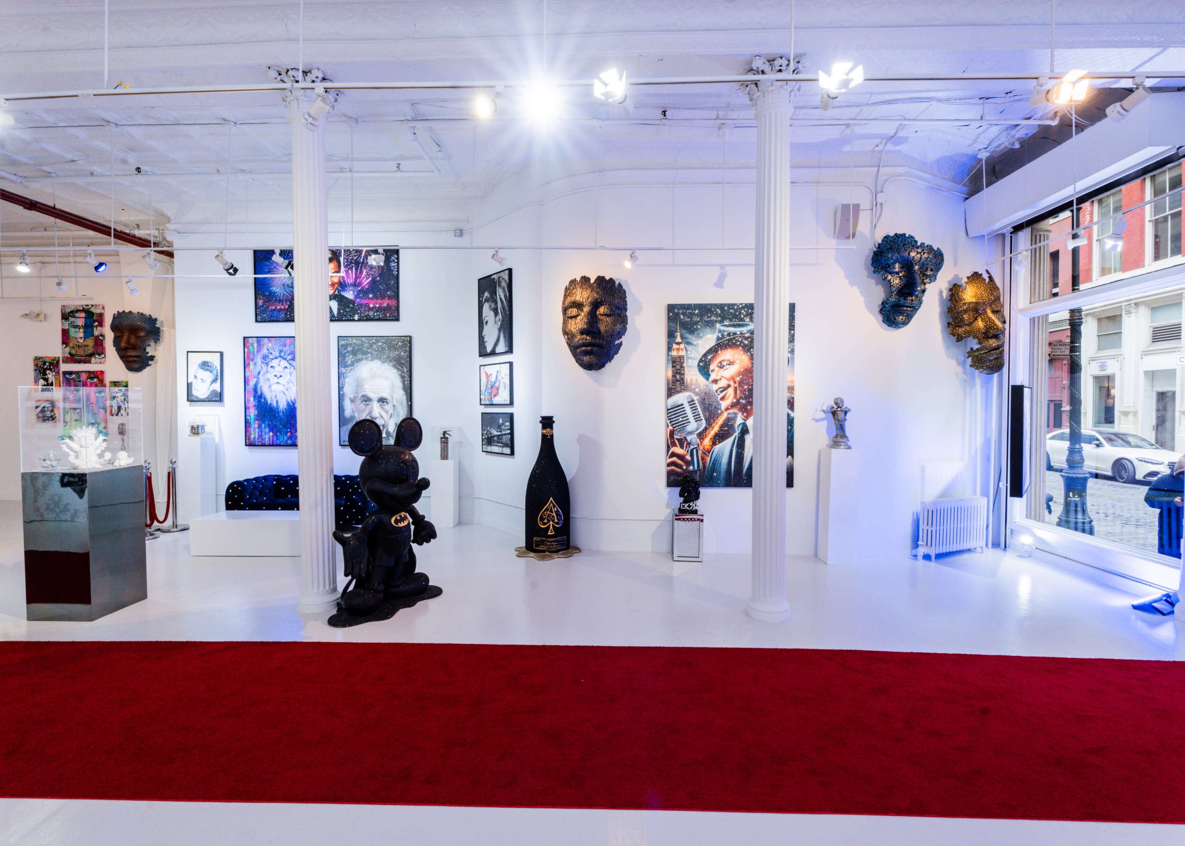 The image shows an art gallery featuring various sculptures and paintings, with a red carpet running through the center and large windows allowing natural light.