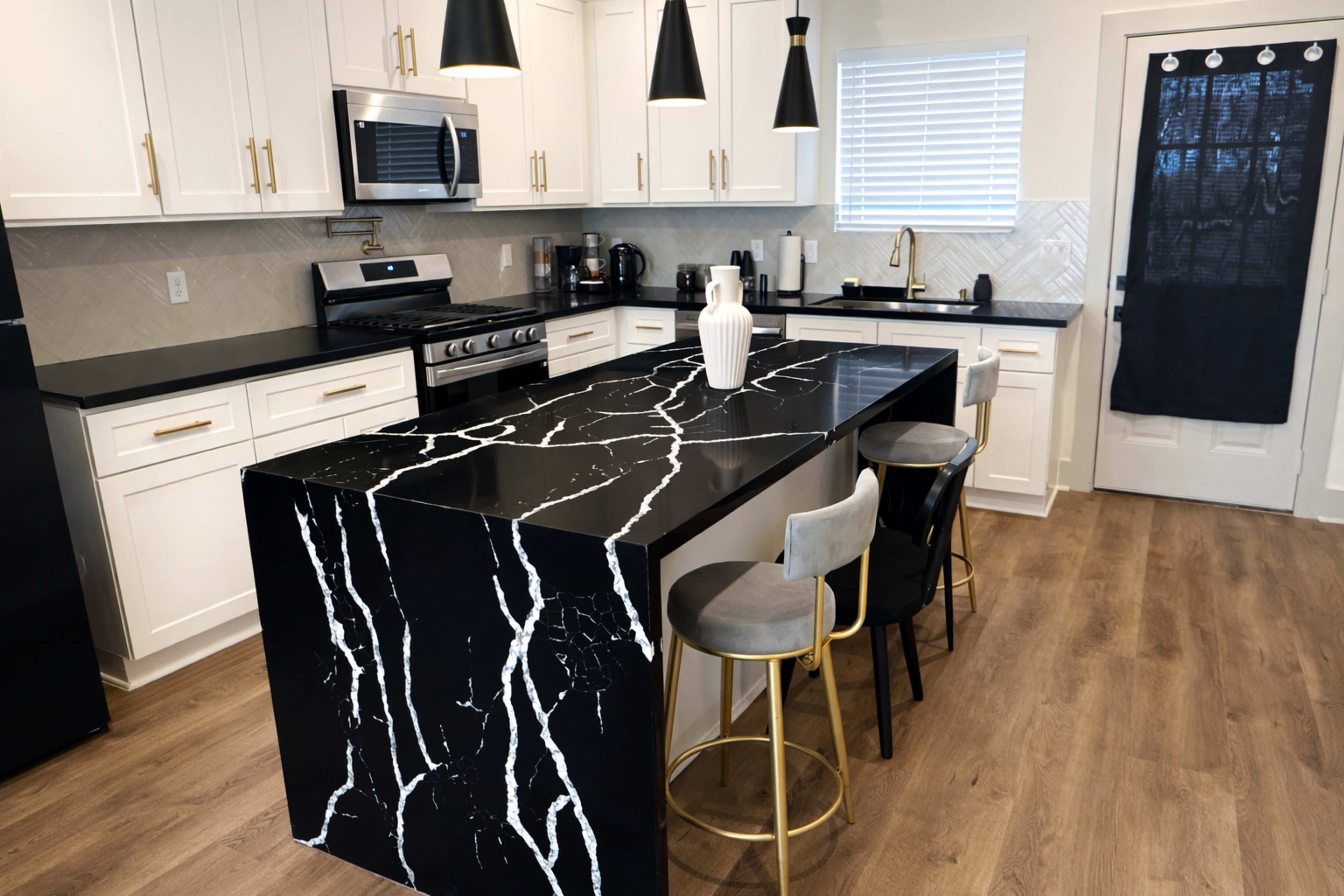 A modern kitchen features white cabinetry, a black marble island with dramatic white veins, and stainless steel appliances, with seating at the island.