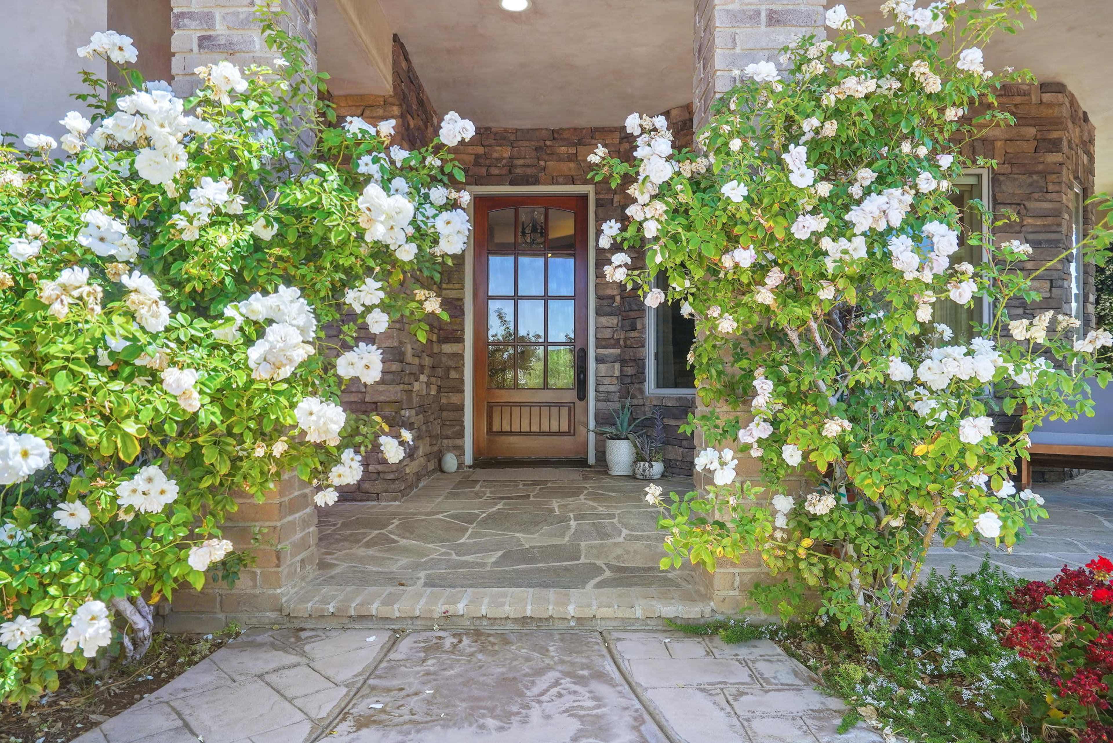 The image shows a stone porch with white flowering plants flanking a wooden front door.