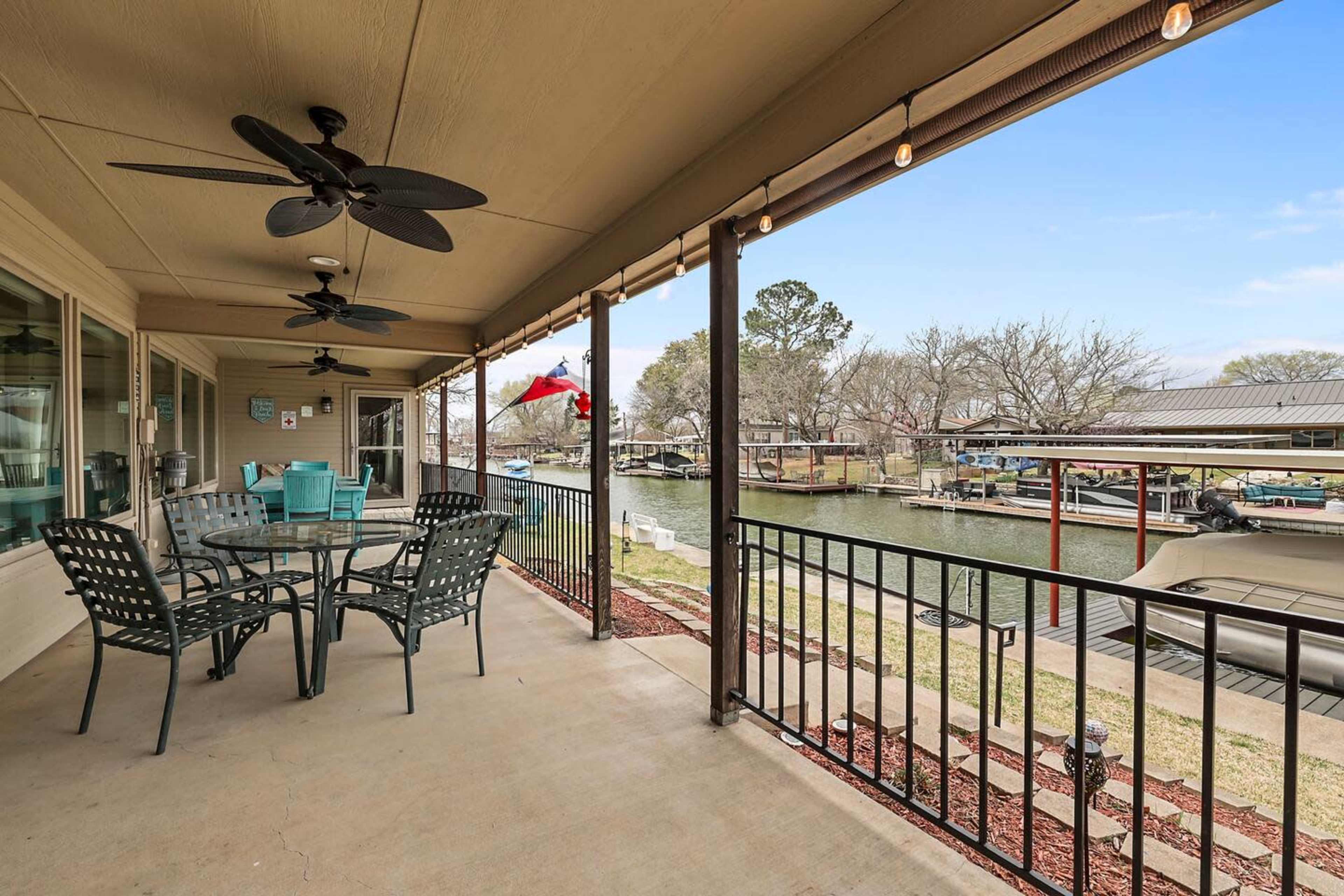 A covered patio features a dining table and chairs overlooking a canal with boats moored alongside.