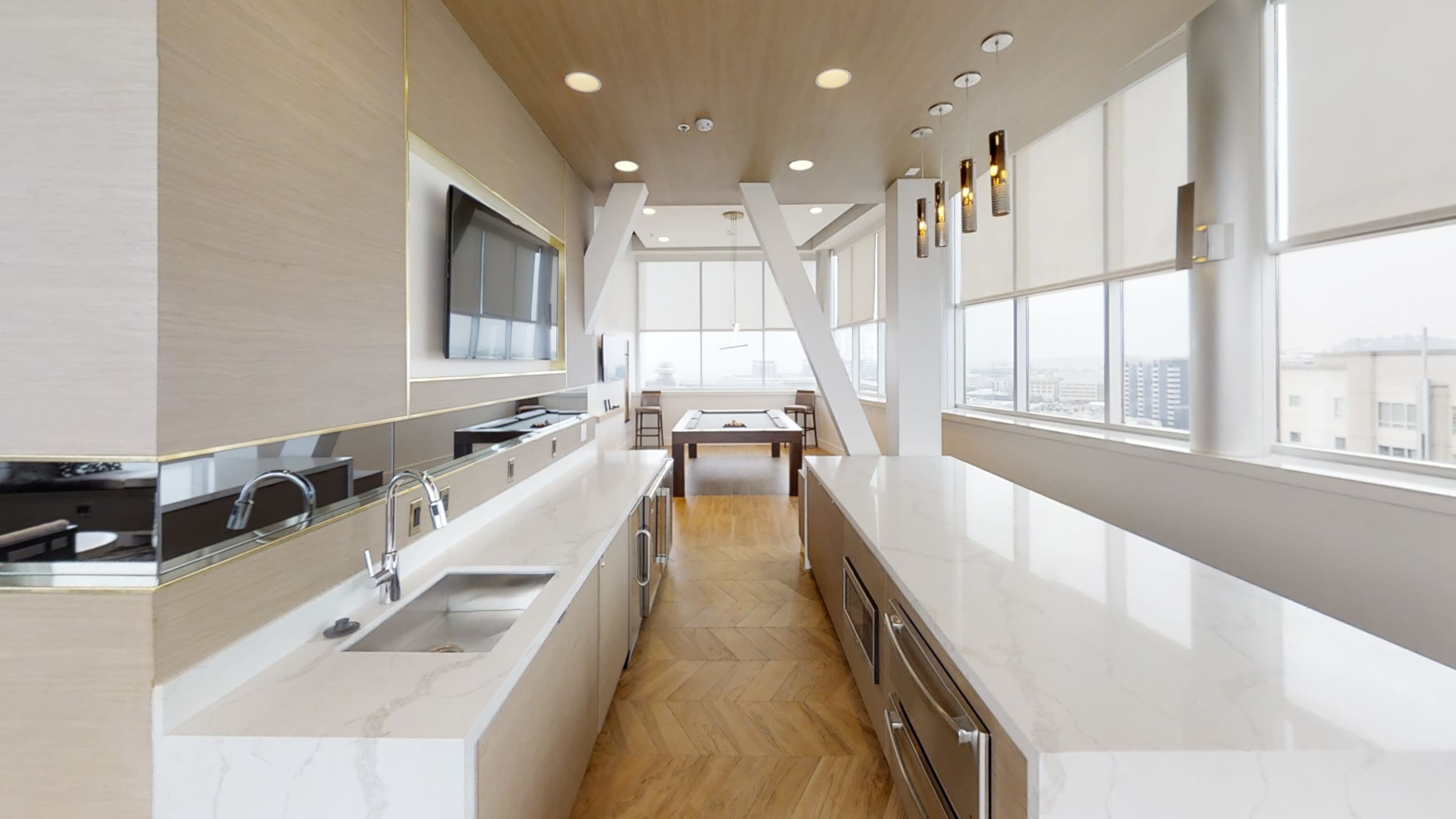A modern kitchen with a long island counter, sleek cabinetry, and large windows offering city views.