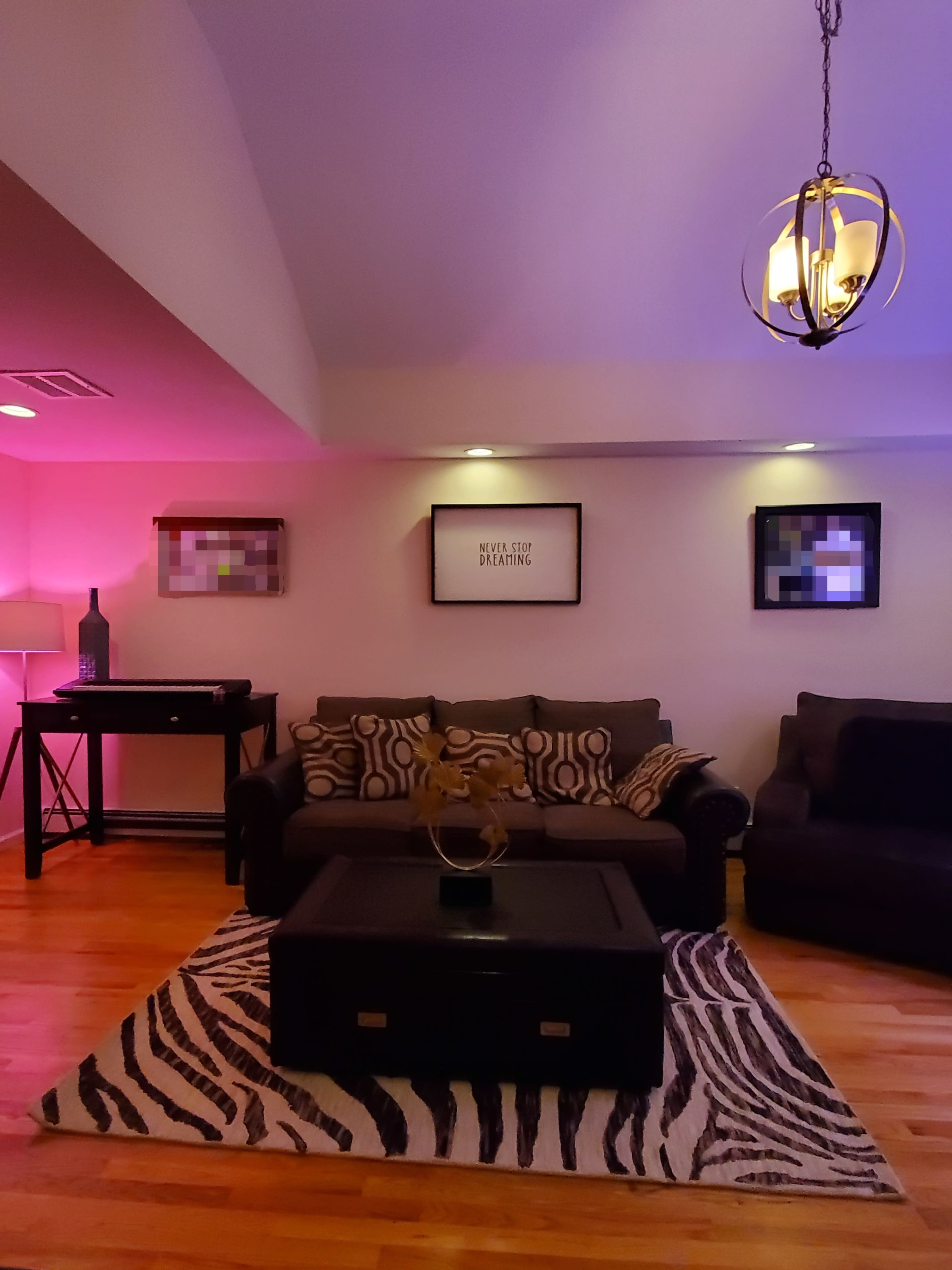A living room features a dark sofa and a coffee table on a zebra-patterned rug, illuminated by soft colored lighting.