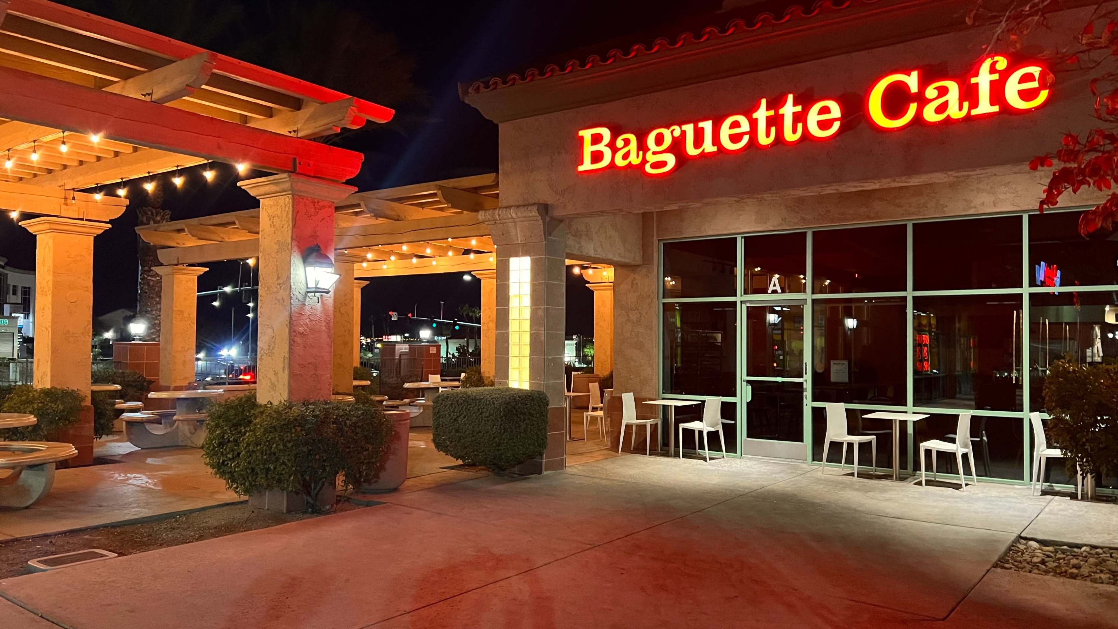 The exterior of Baguette Cafe illuminated at night, with outdoor seating and decorative lights.