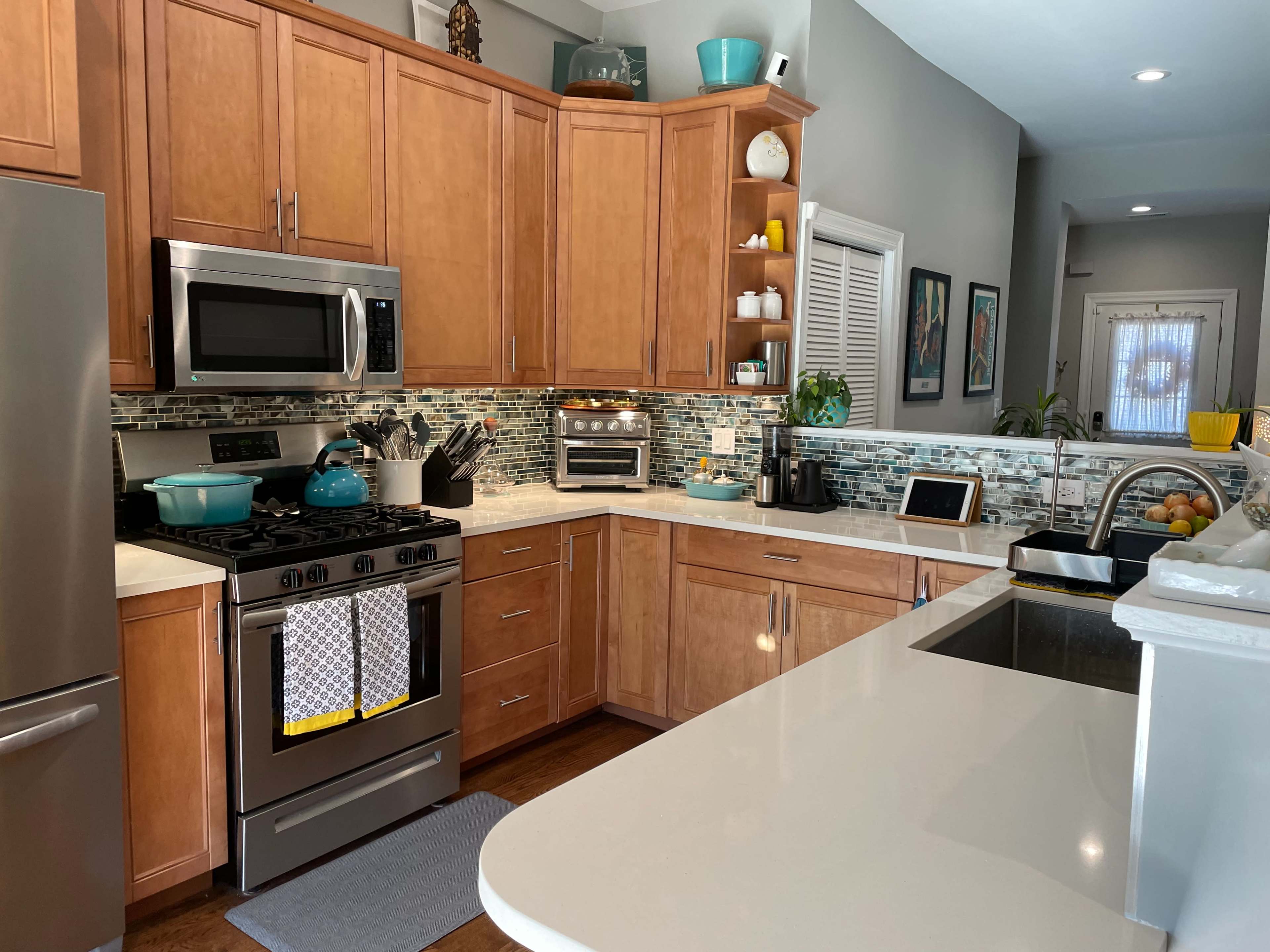 A modern kitchen with wooden cabinetry, stainless steel appliances, and a gray countertop, featuring a mosaic tile backsplash.