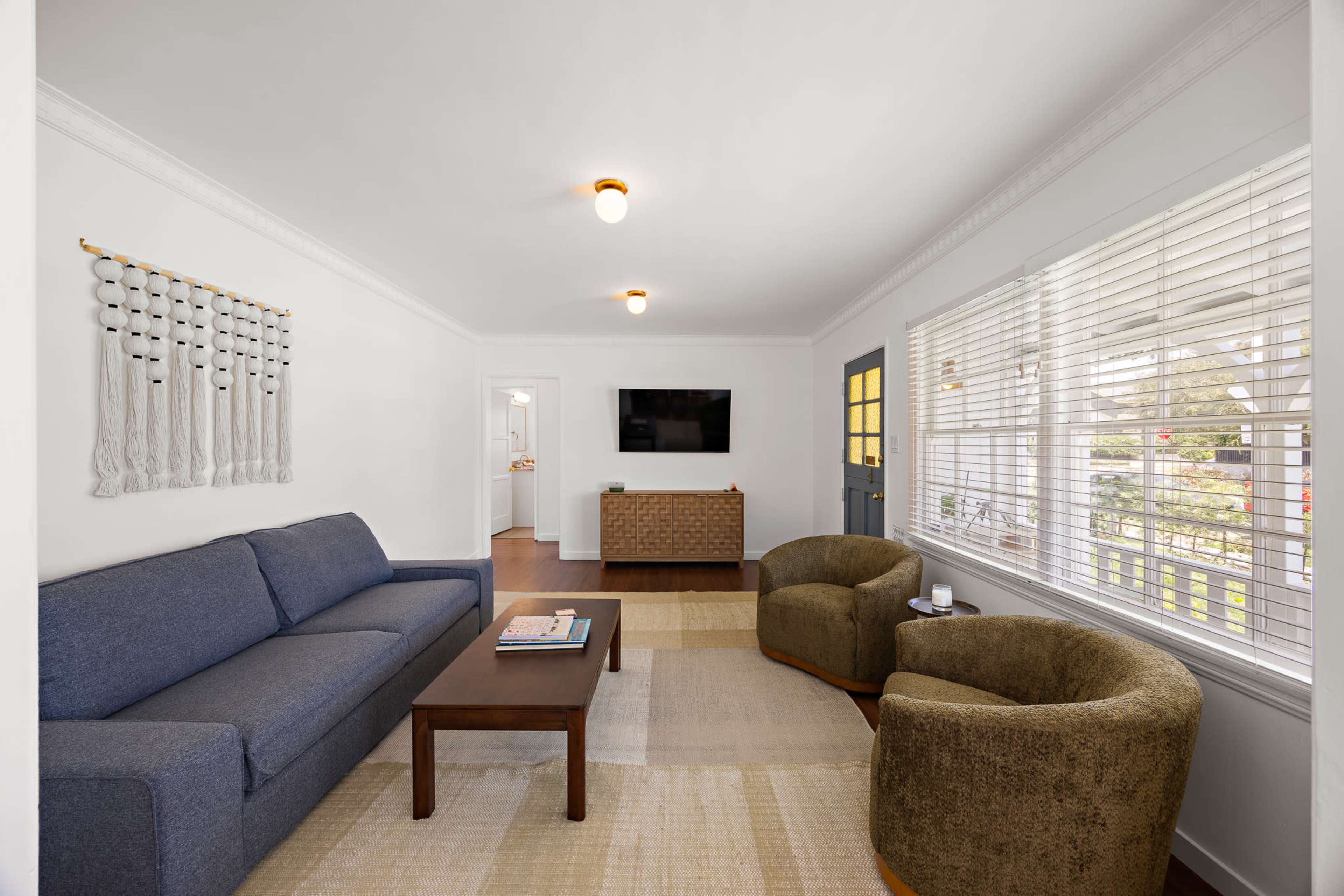 A cozy living room features a blue sofa, two green chairs, a wooden coffee table, and a television mounted on the wall.