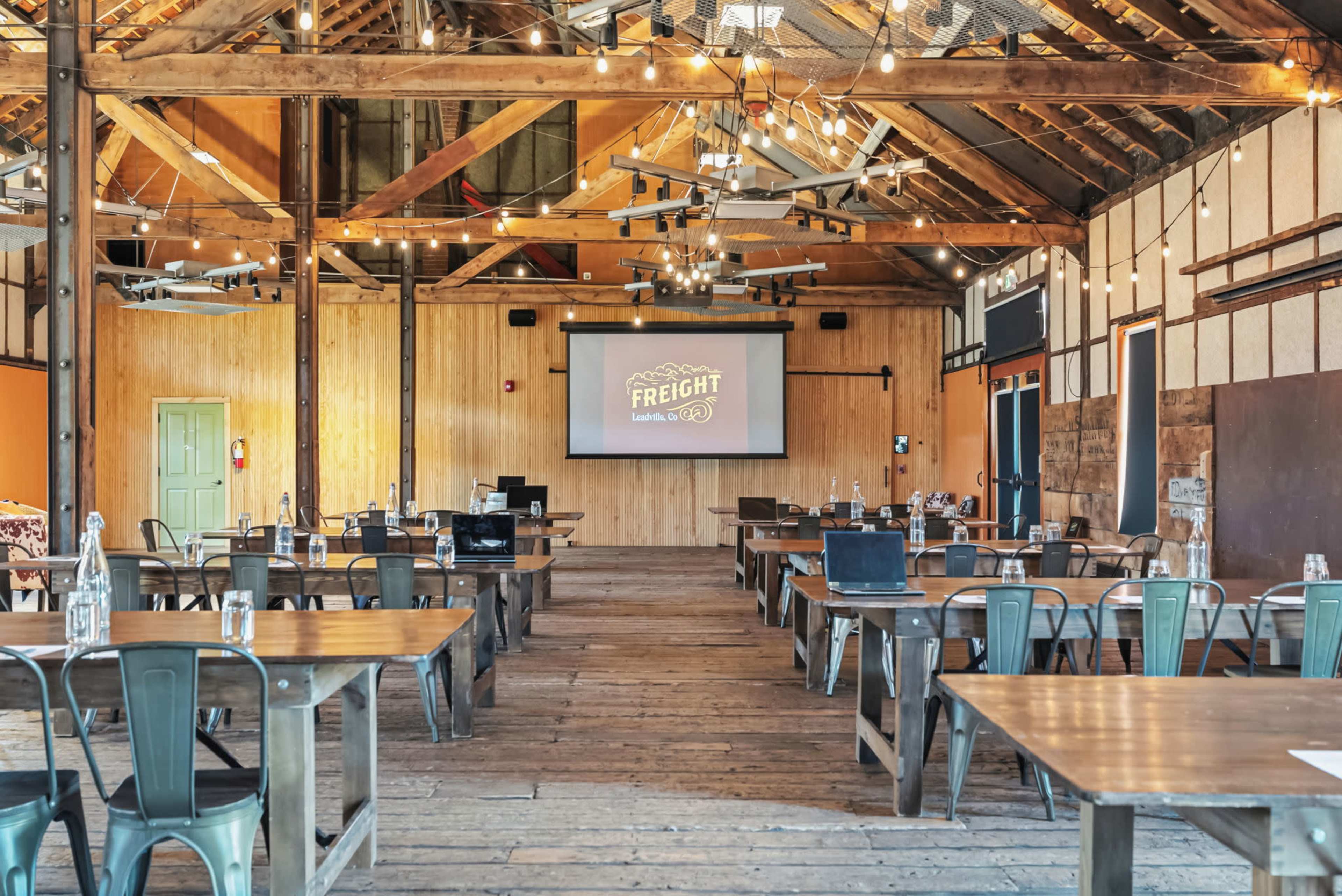 The image shows a spacious meeting room with wooden flooring, tables arranged in a classroom style, and a large screen displaying the word "FREIGHT" in the front.