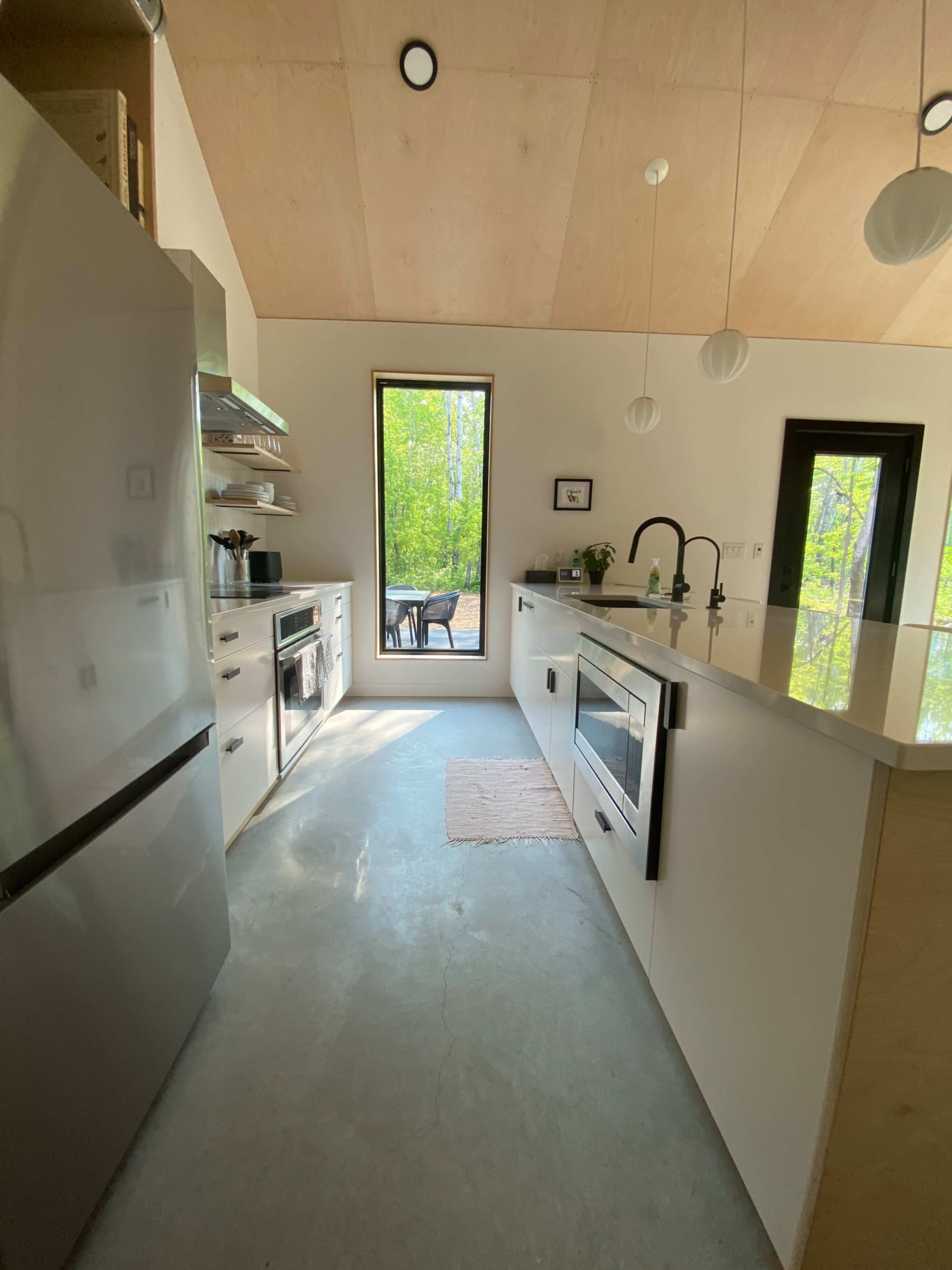 A modern kitchen features sleek cabinetry, stainless steel appliances, and a large window overlooking a wooded area.