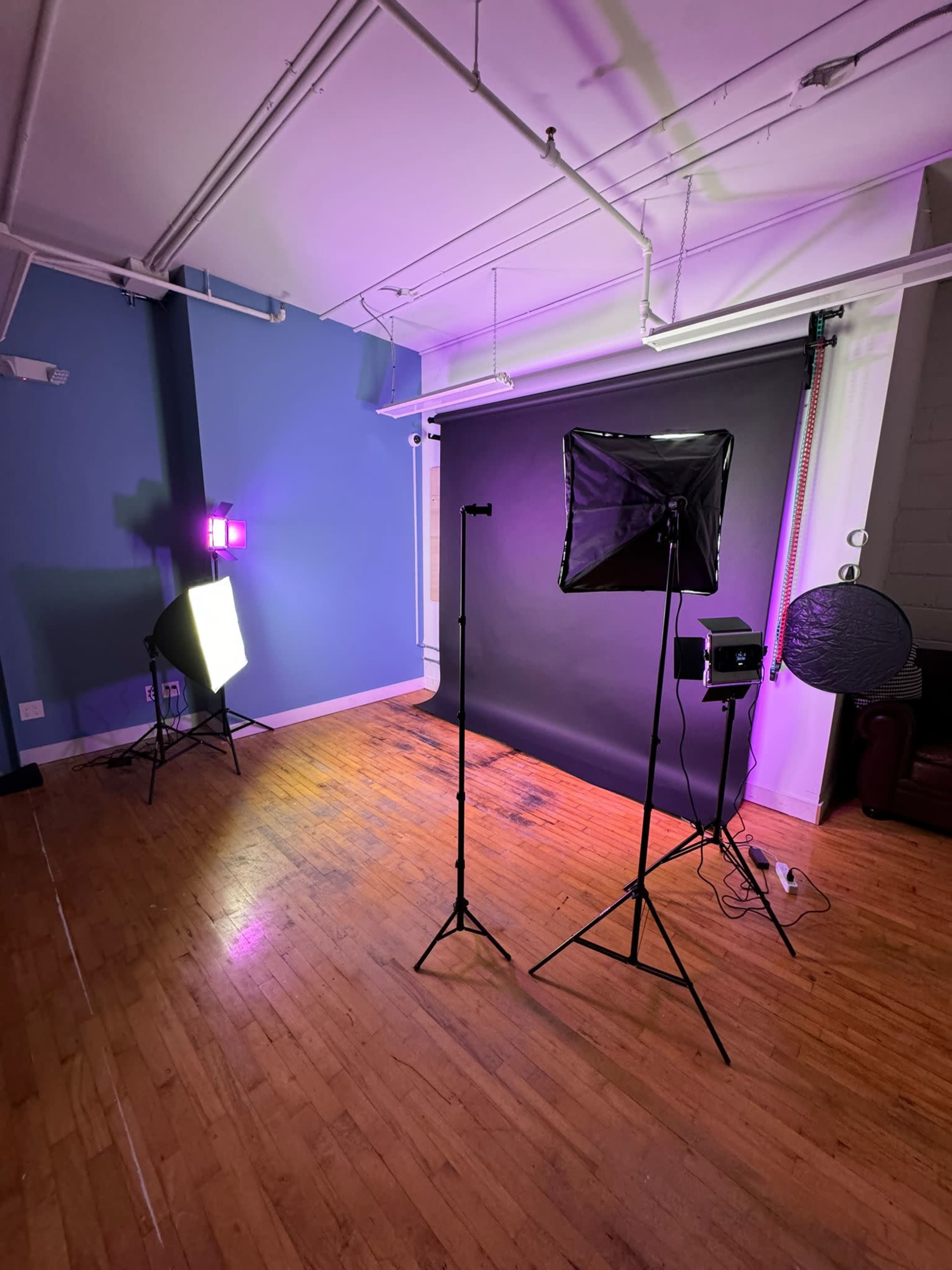 A photography studio featuring backdrop stands, lighting equipment, and wooden flooring.