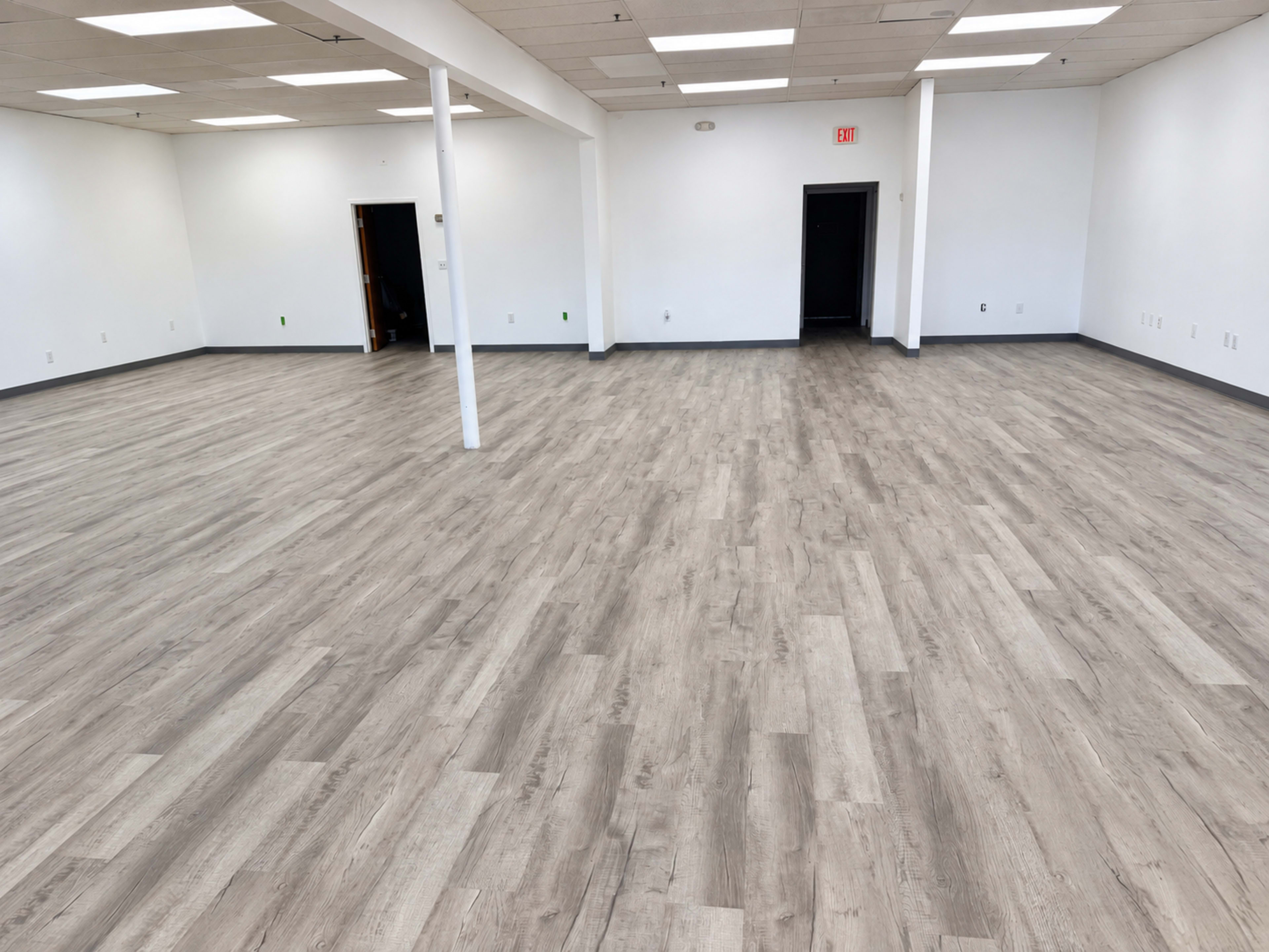 The image shows an empty room with light wood laminate flooring, white walls, and multiple doors leading to other spaces.