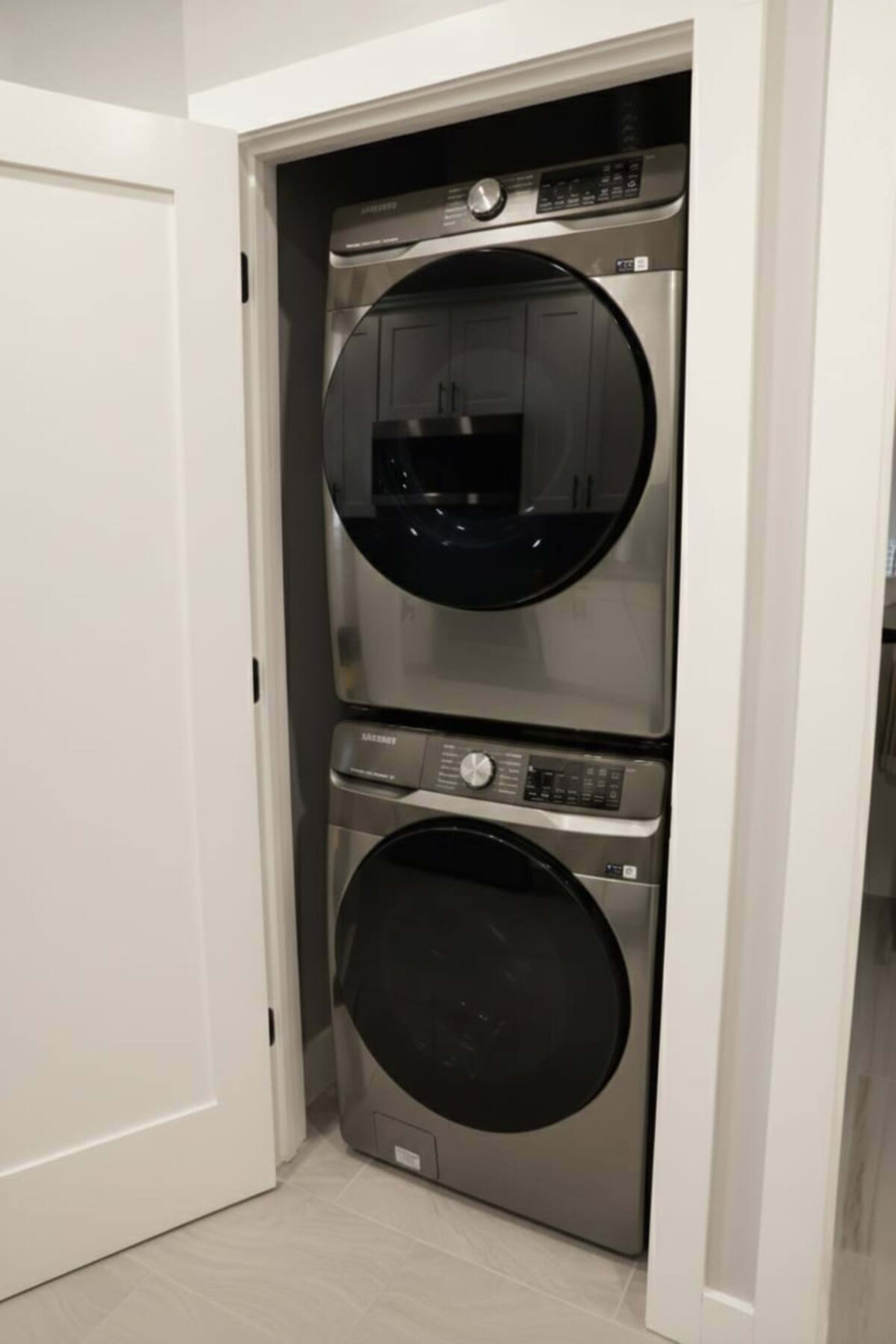 The image shows a stacked set of modern, metallic washer and dryer units installed inside a small closet space.